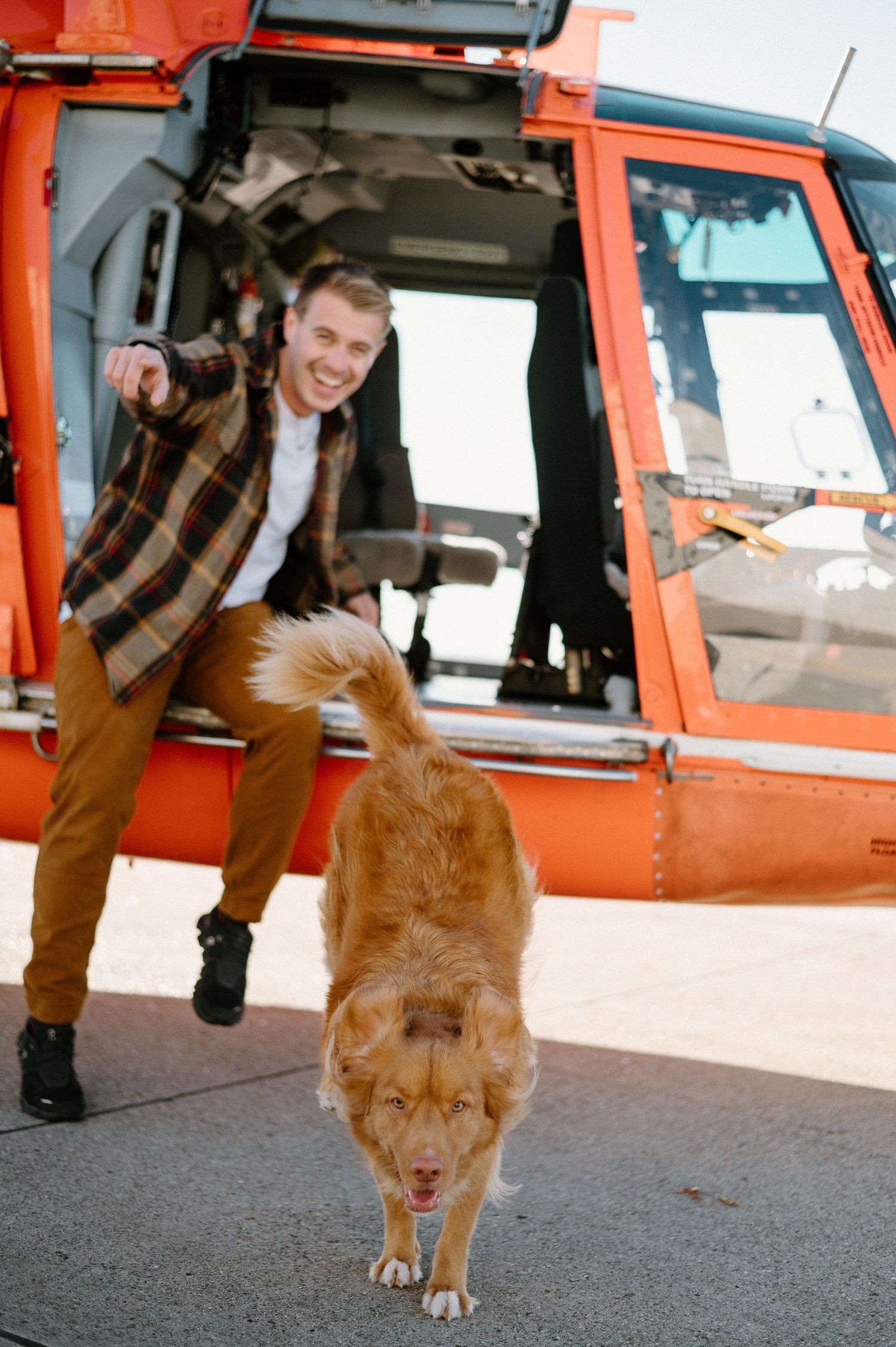 Person and dog pose next to orange Coast Guard helicopter on tarmac.