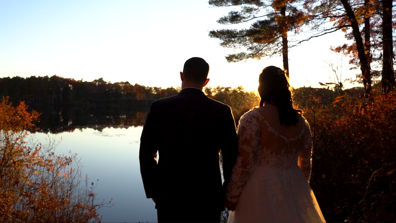 Silhouetted figures stand against a sunset backdrop during an outdoor wedding ceremony.