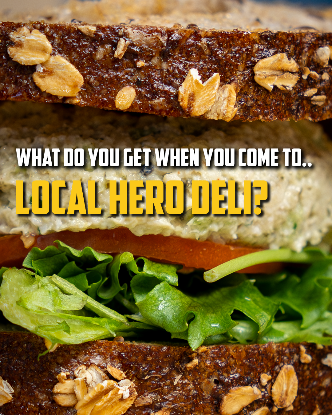Close-up of a hearty sandwich on multigrain bread with lettuce and tomato, promoting Local Hero Deli.