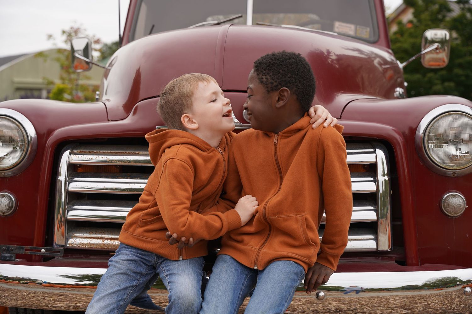 Two children share a moment while sitting on vintage red truck.