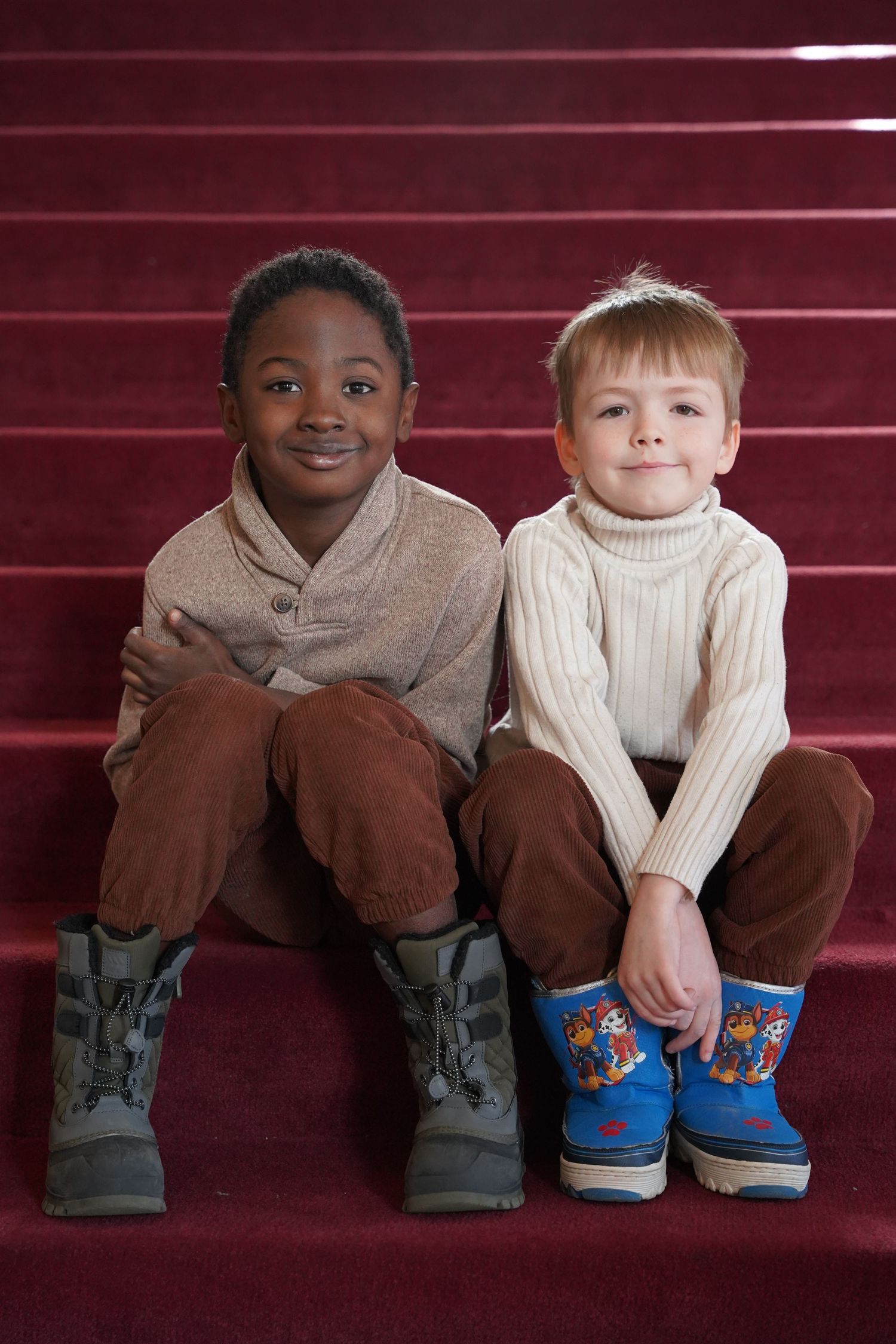Two children sit on red steps showing off their colorful socks and shoes.