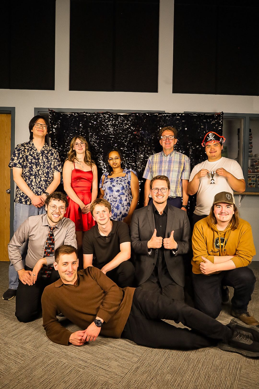 Group of ten young adults posing together in front of a black sequined backdrop at a formal event.