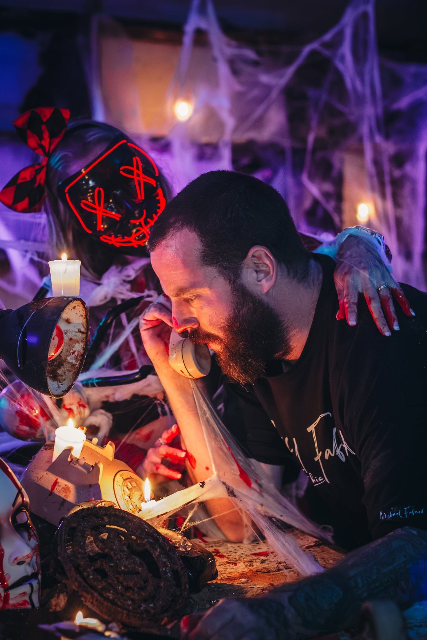 People in Halloween decor setting with cobwebs and red lighting examining objects.