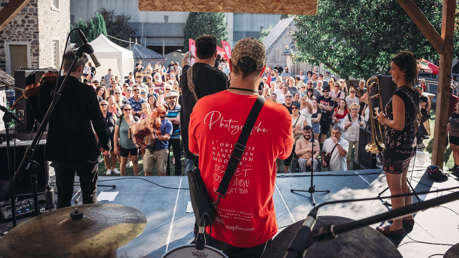 Outdoor festival scene with crowds and stage equipment under bright sunlight.