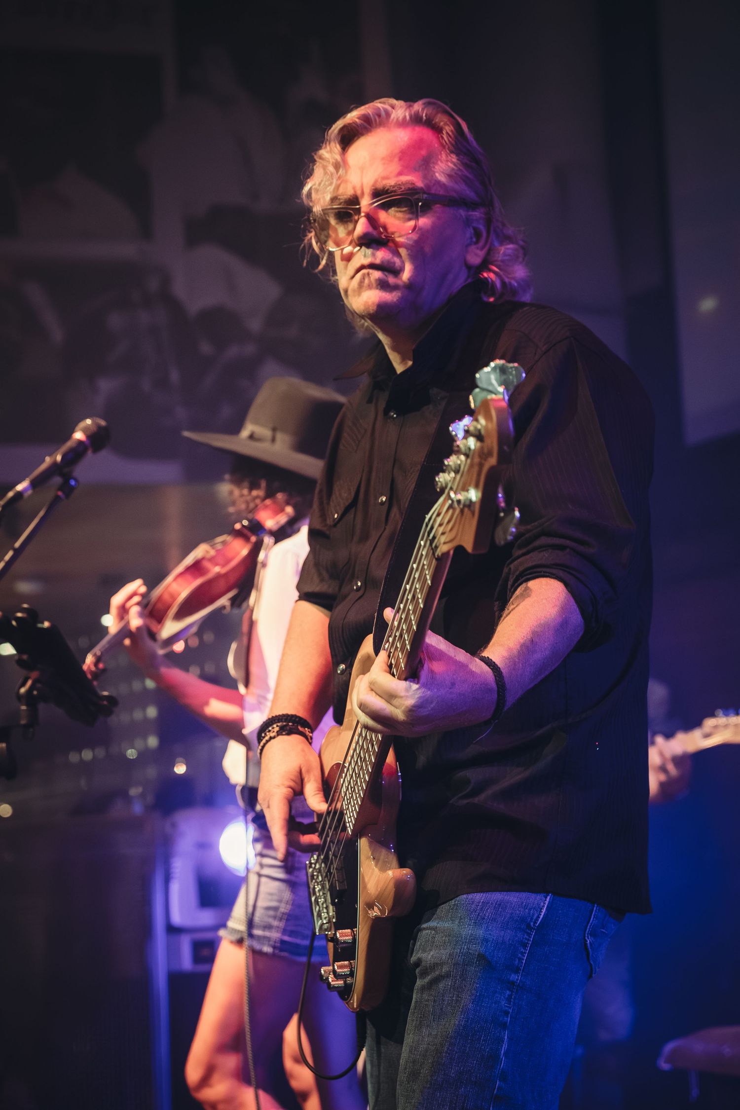 Bass guitarist performing on stage with purple and blue lighting effects.