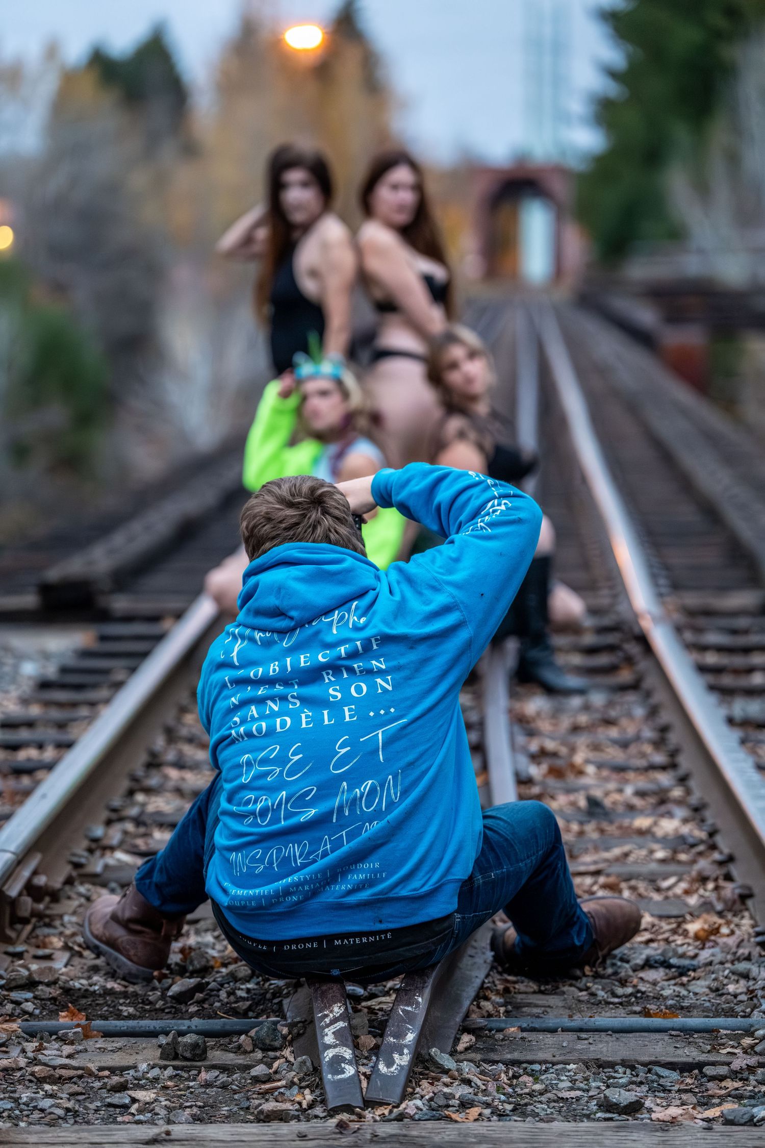 Photographer in blue shirt taking creative shots on railway tracks at dusk.