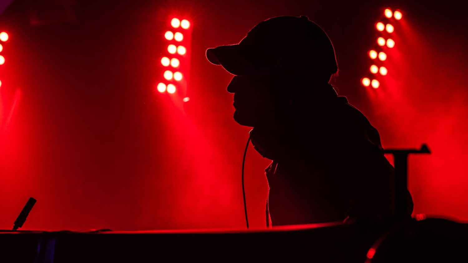 Silhouetted figures perform on stage against dramatic red lighting and fog effects during a concert performance.