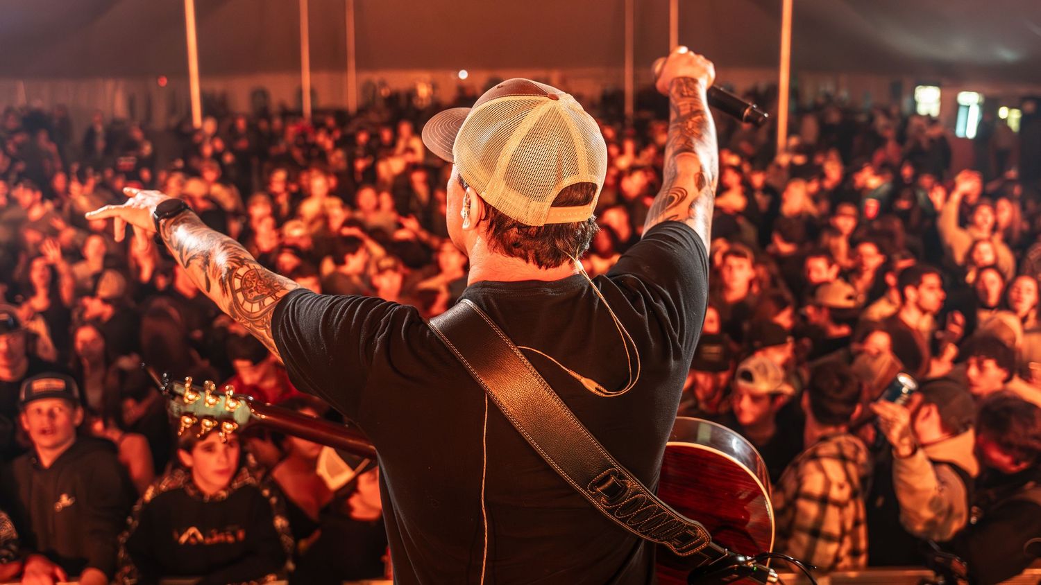 Large concert crowd illuminated by orange stage lights during nighttime performance.