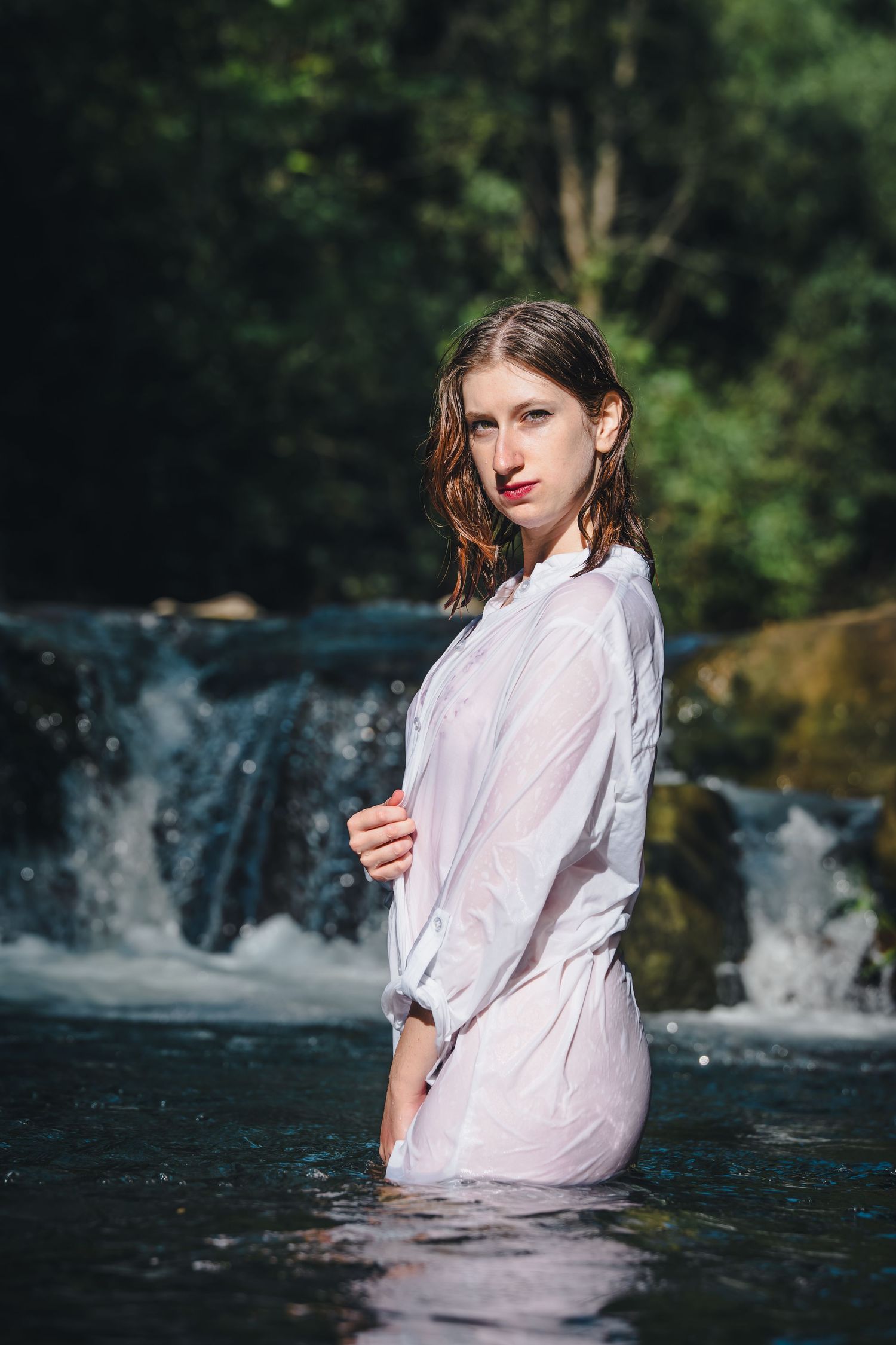 An artistic portrait taken in a flowing stream with a cascading waterfall backdrop.