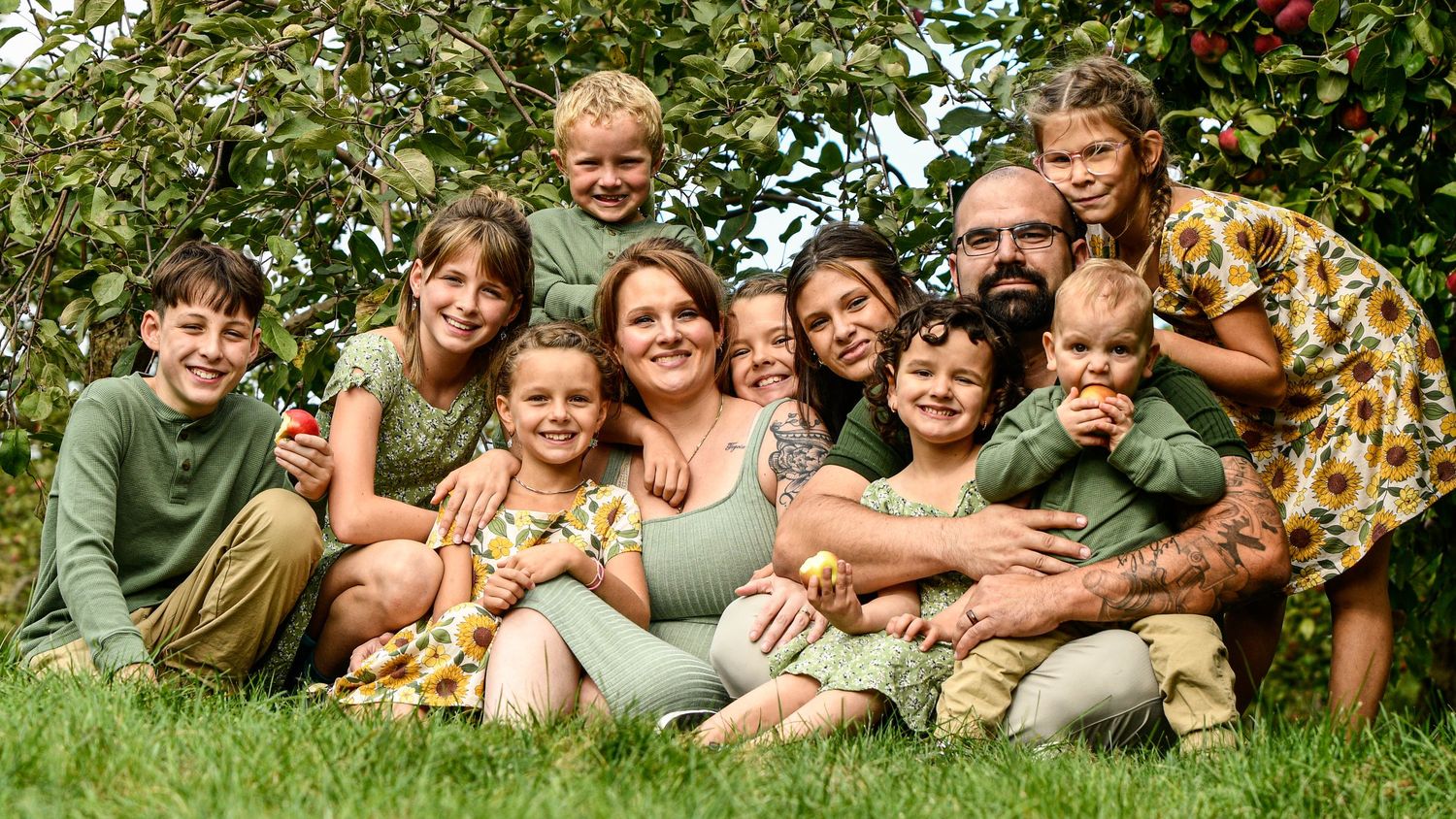 Family group photo taken outdoors with greenery and sunflowers in the background.