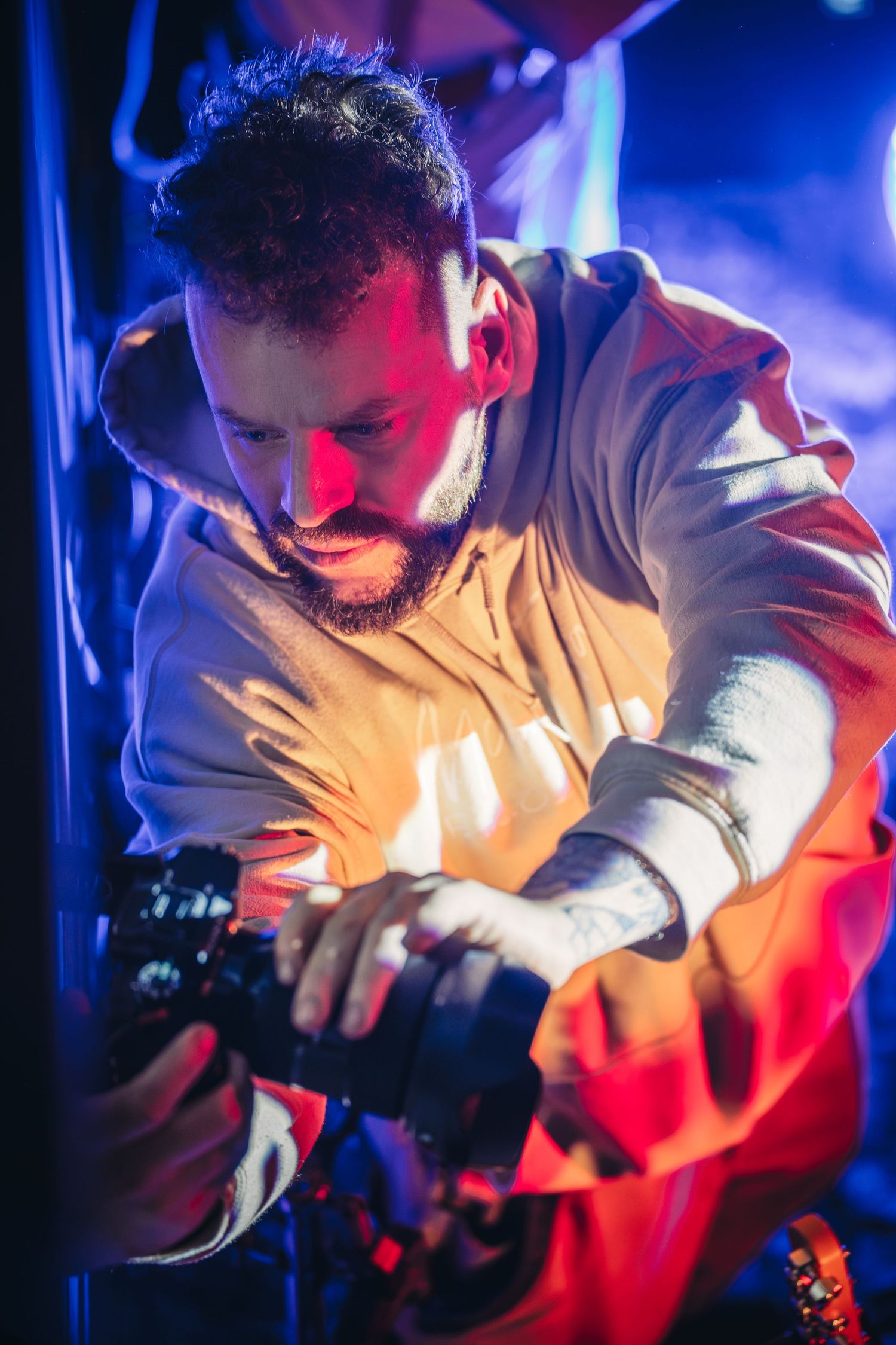 Musician in light-colored hoodie performing with dramatic blue and red stage lighting.