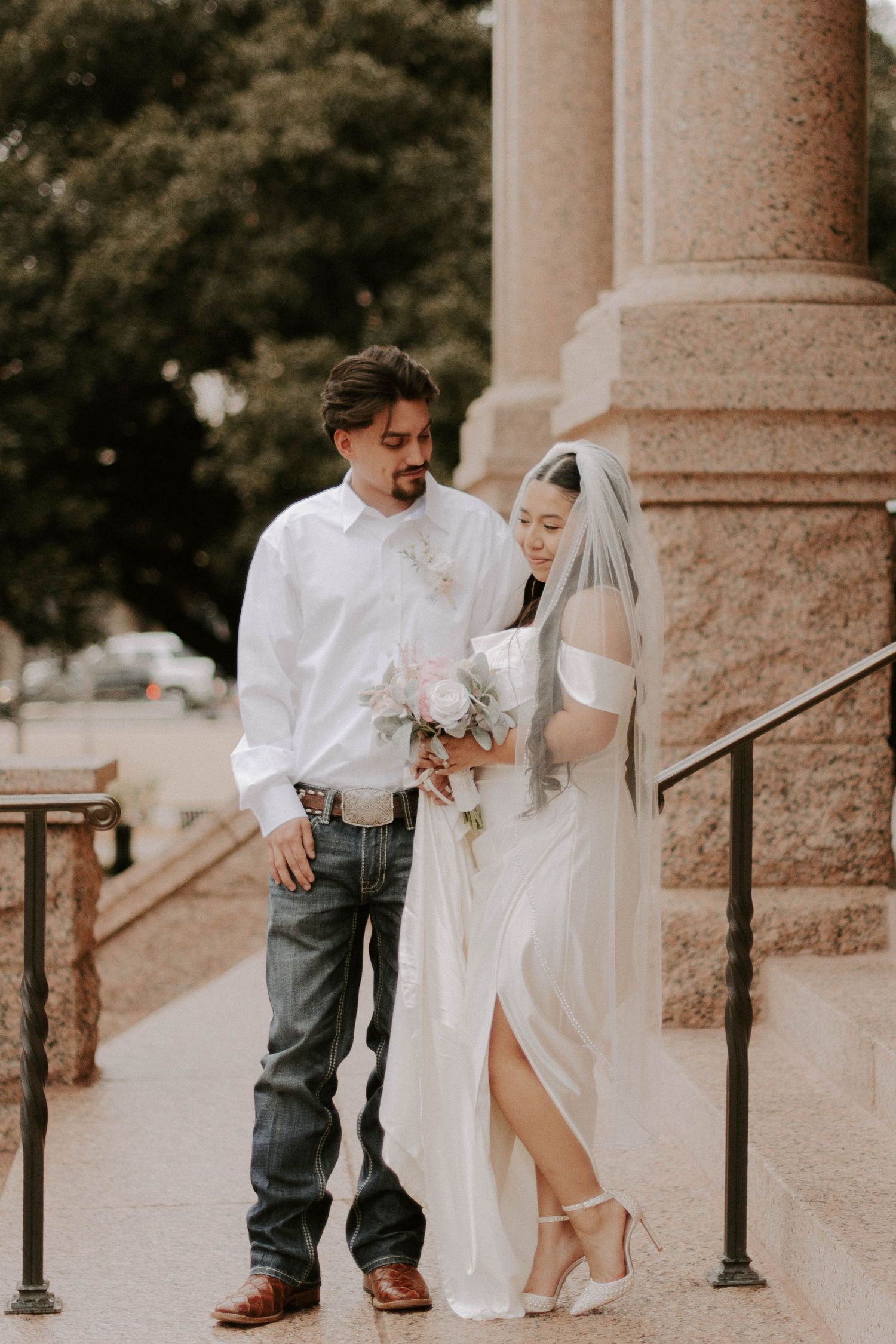 A wedding couple poses on stone steps outside a historic building with classic architecture.