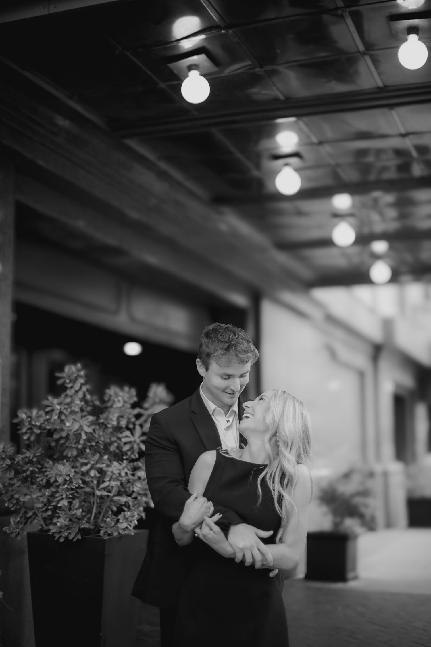 A romantic black and white photo series of a couple dancing together in an indoor venue with soft lighting.