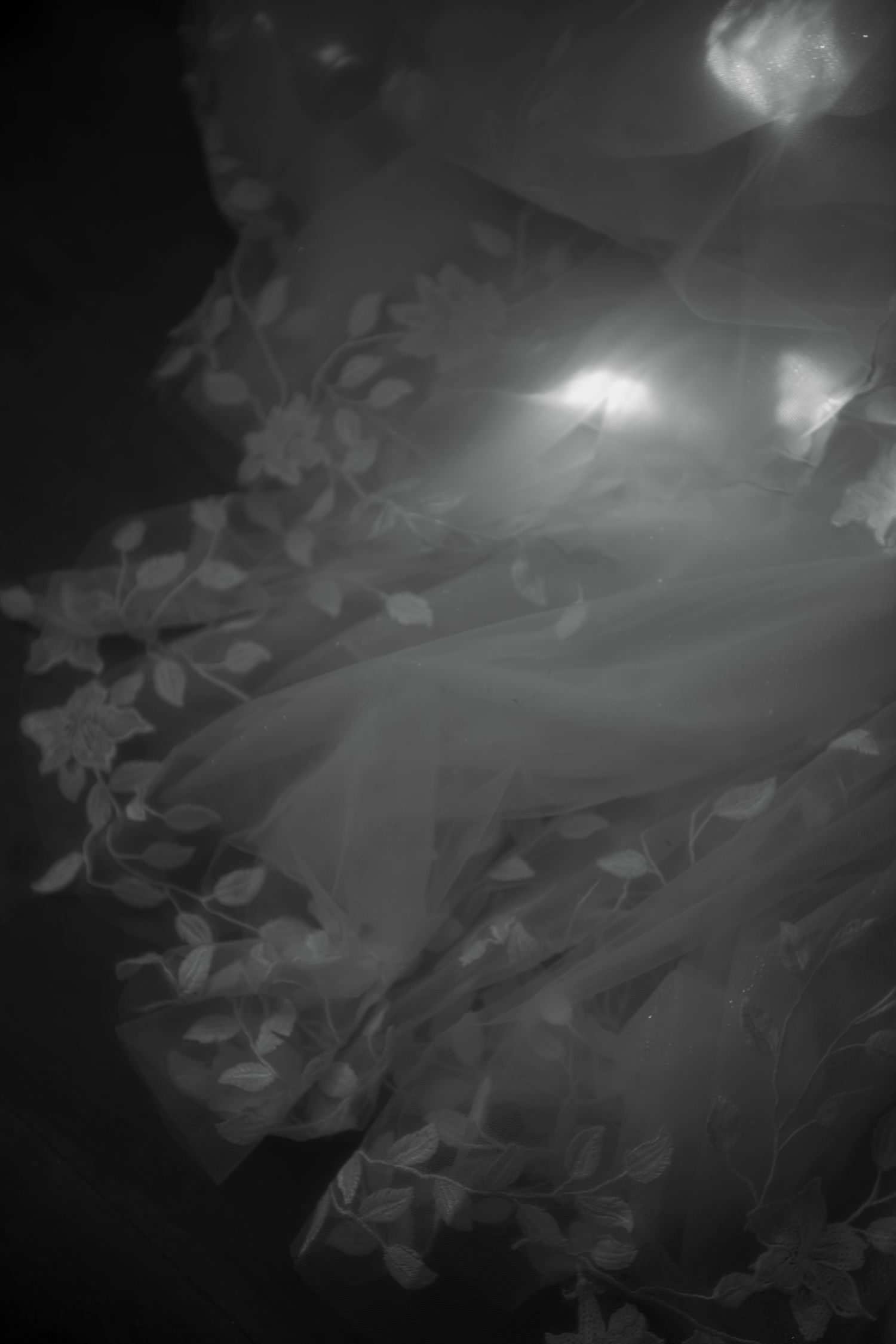 Artistic black and white detail shot of wedding dress lace and fabric in dramatic lighting.