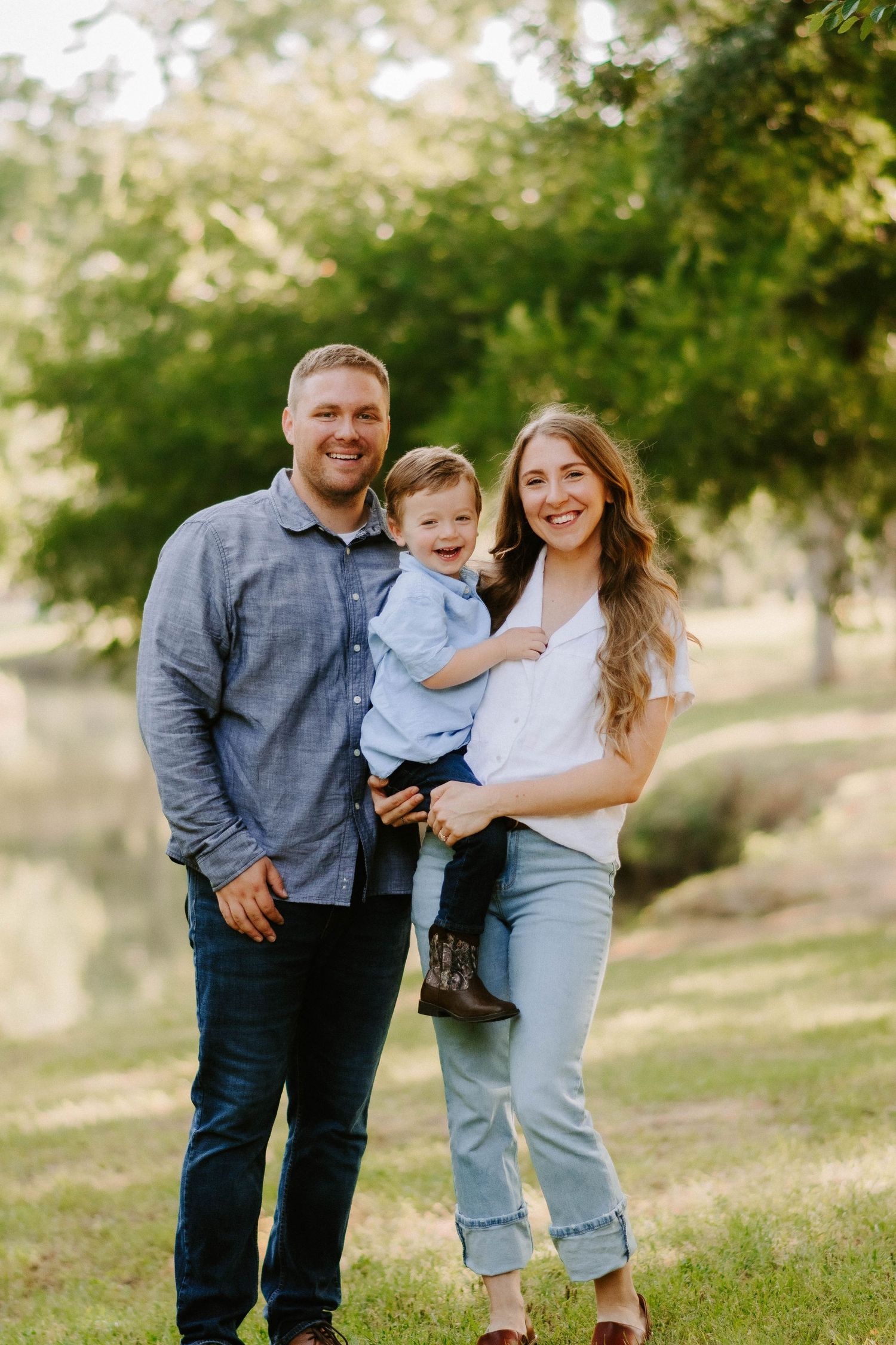 A family enjoys a playful outdoor photo session together on a grassy hill under trees.