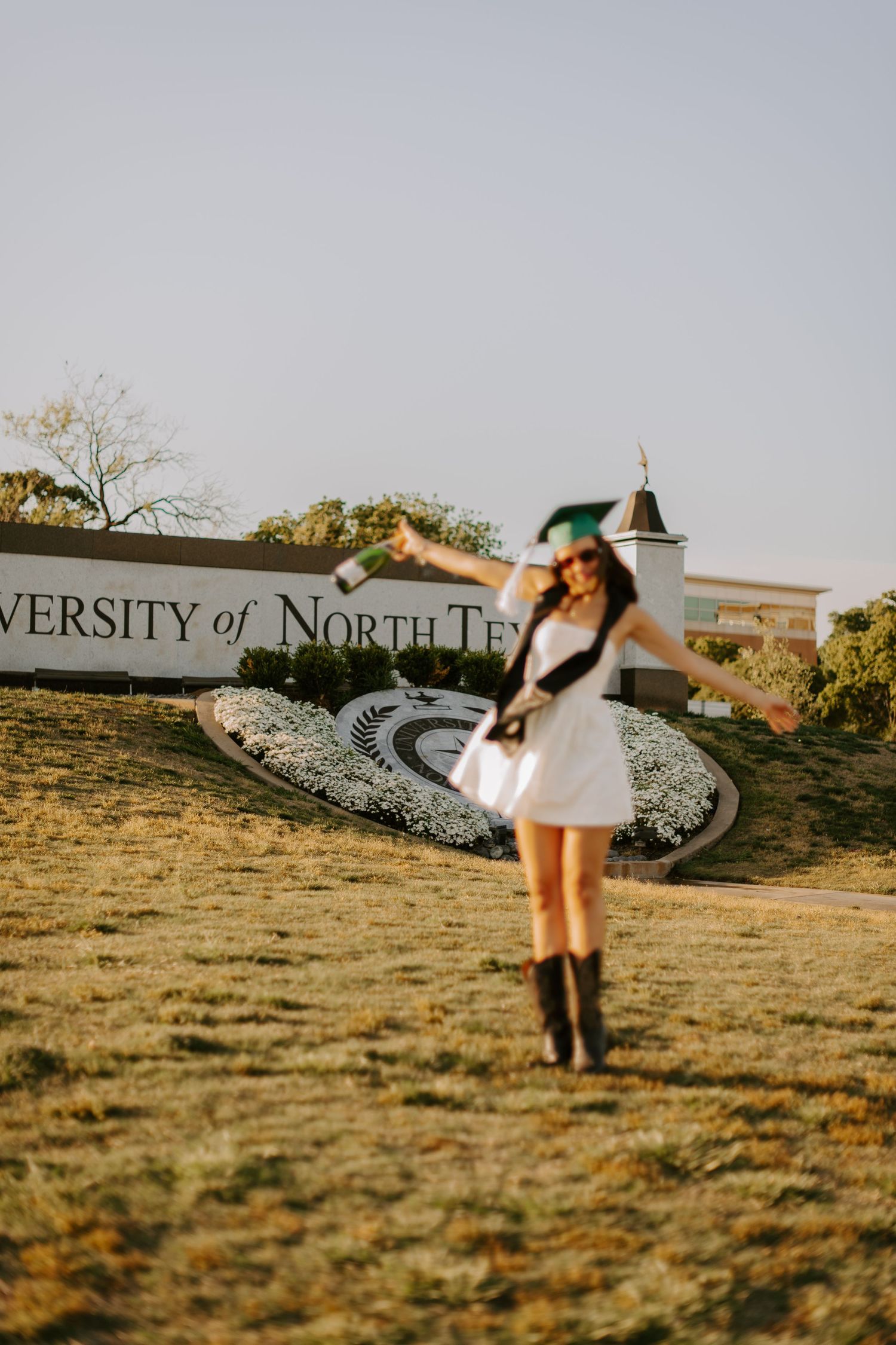Celebratory graduation photo at University of North Texas campus entrance sign.