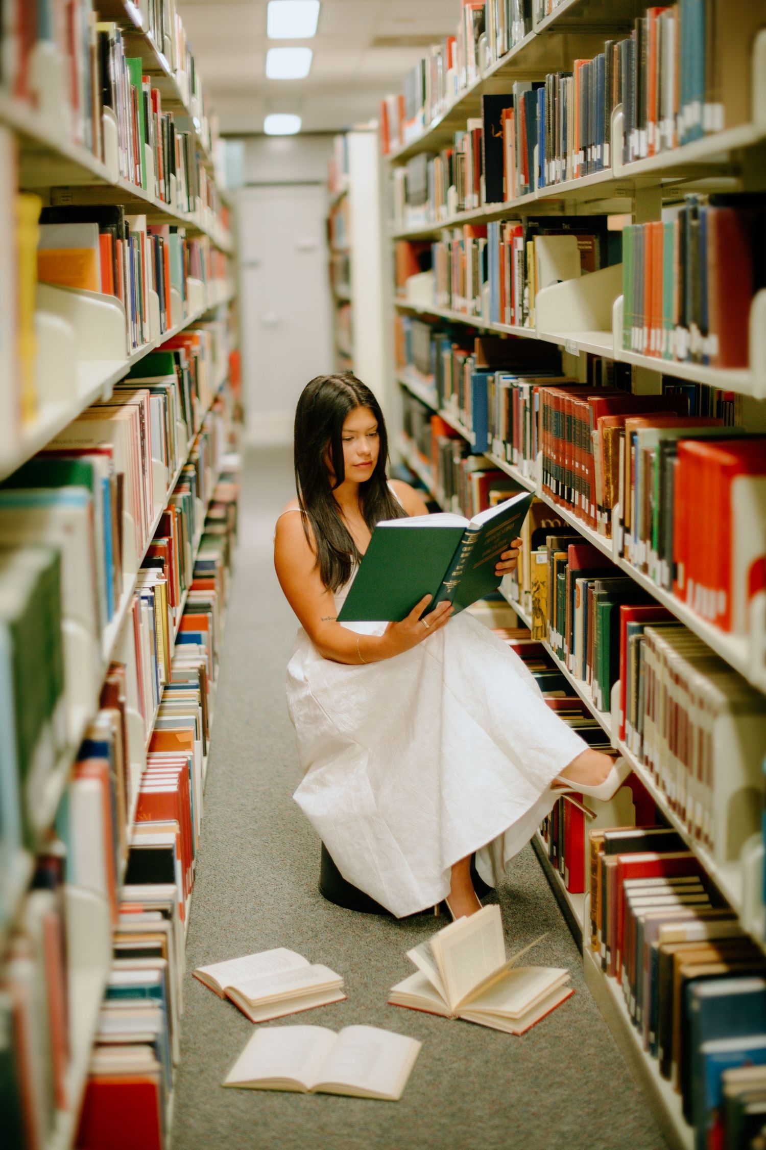 Student browses library shelves while studying and taking notes among rows of academic books in university library.