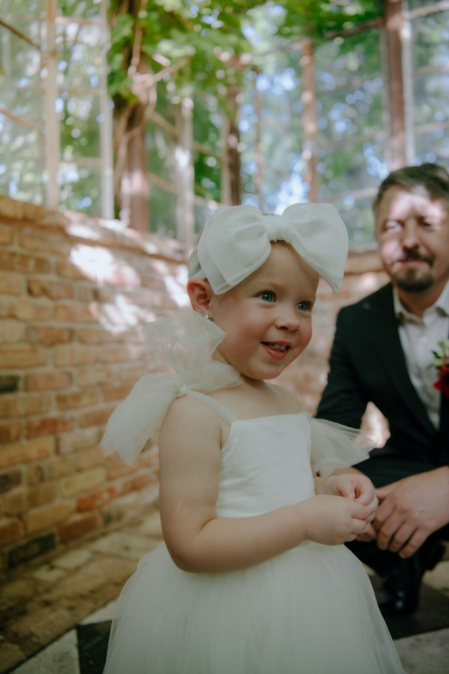 A small child in a white formal dress smiles during a special occasion.