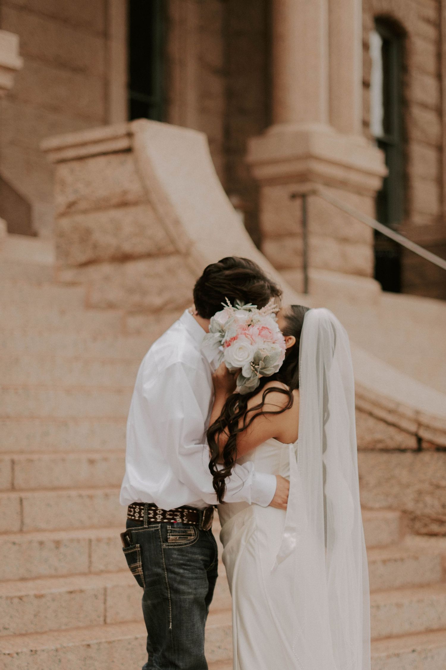 A romantic wedding moment captured on stone steps with a bouquet of pink and white flowers.