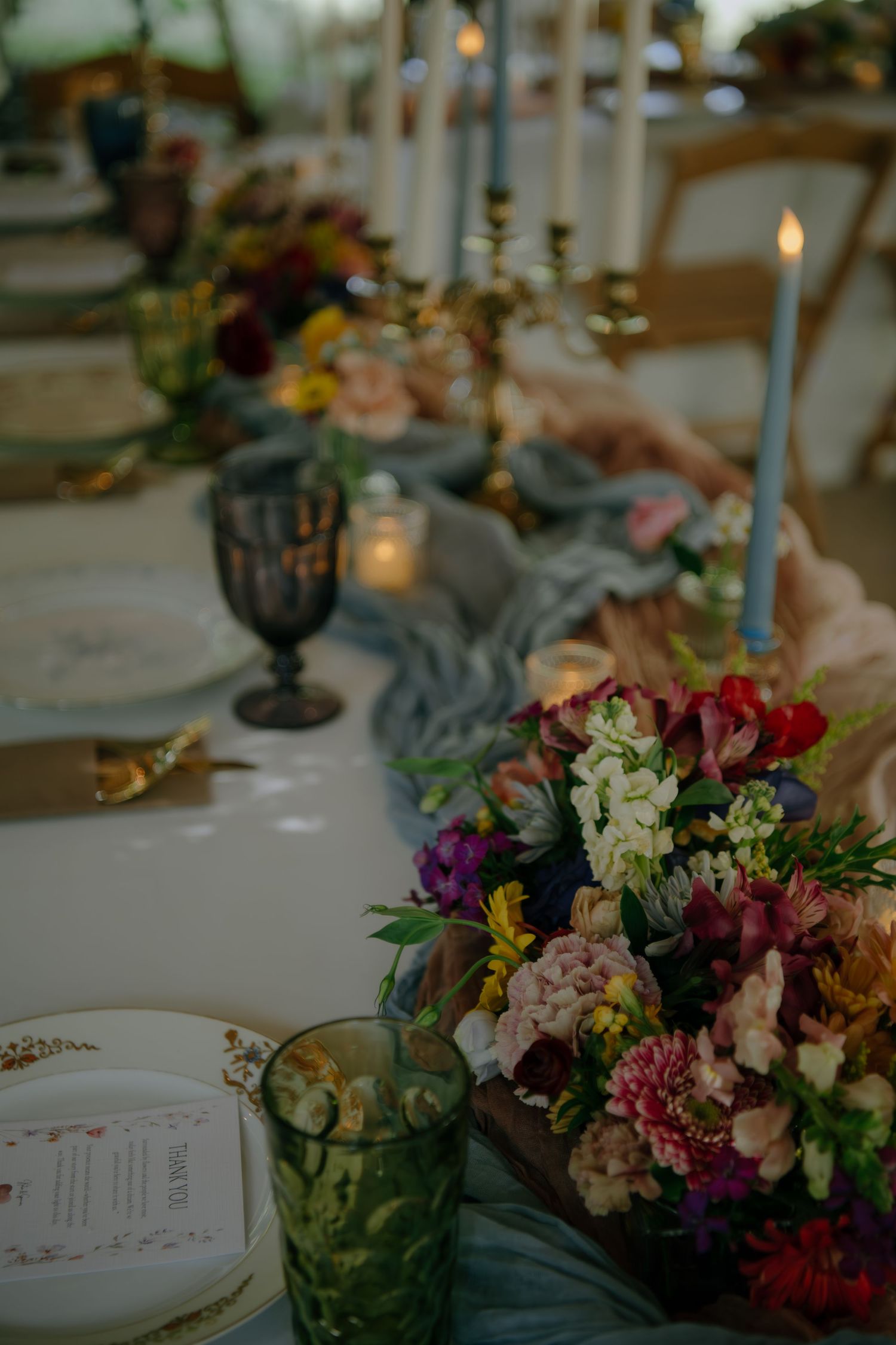 Elegant wedding table setting with colorful floral centerpieces, candles and vintage glassware.