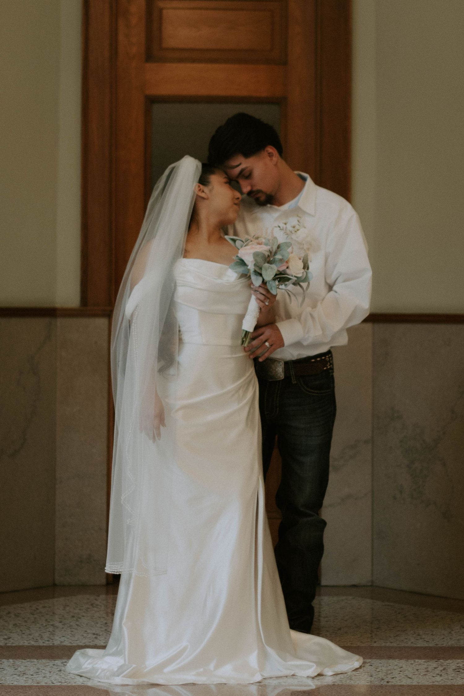 Romantic wedding portrait of couple in white with delicate floral bouquet.