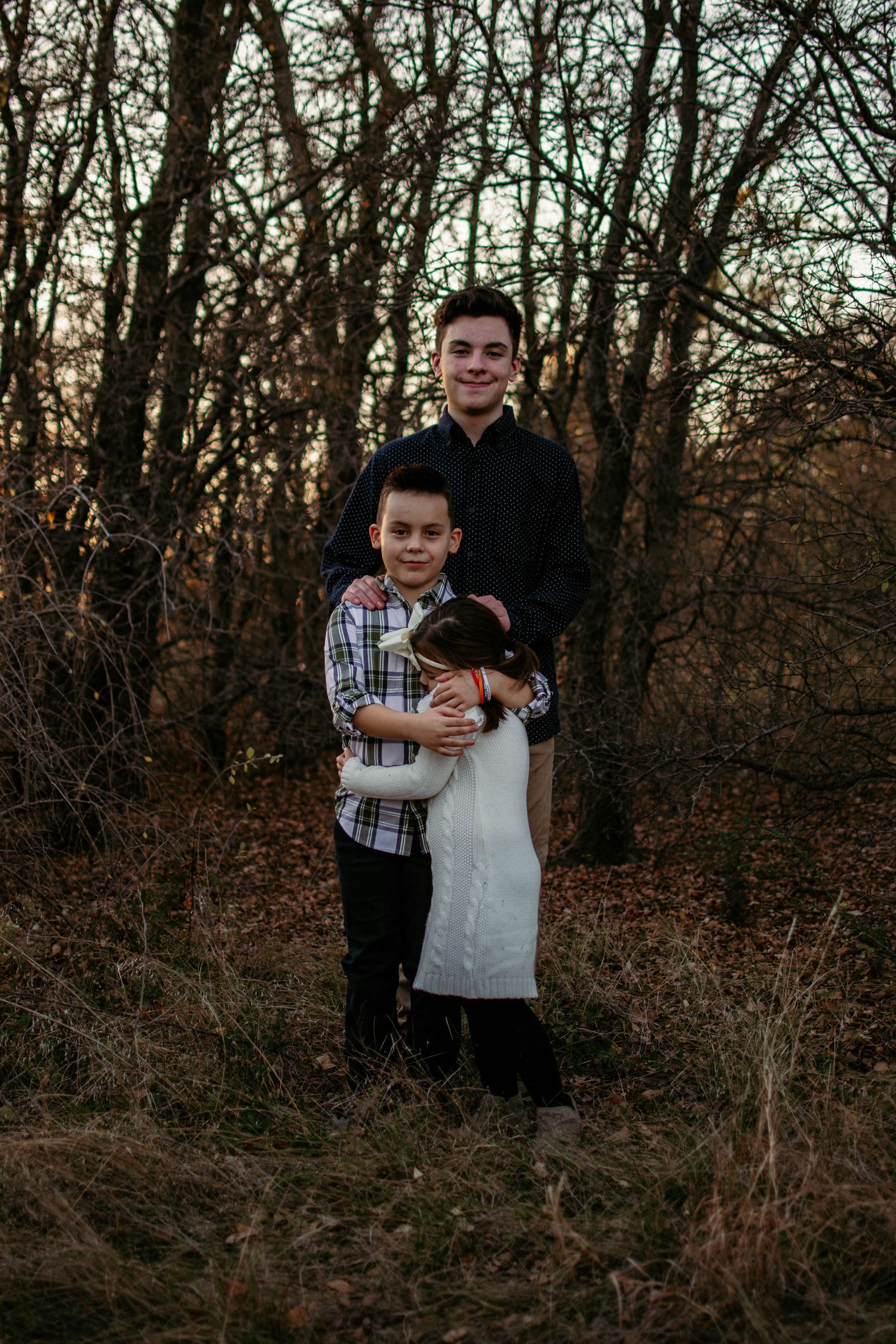 Family group portrait in wooded area during sunset with natural scenery.
