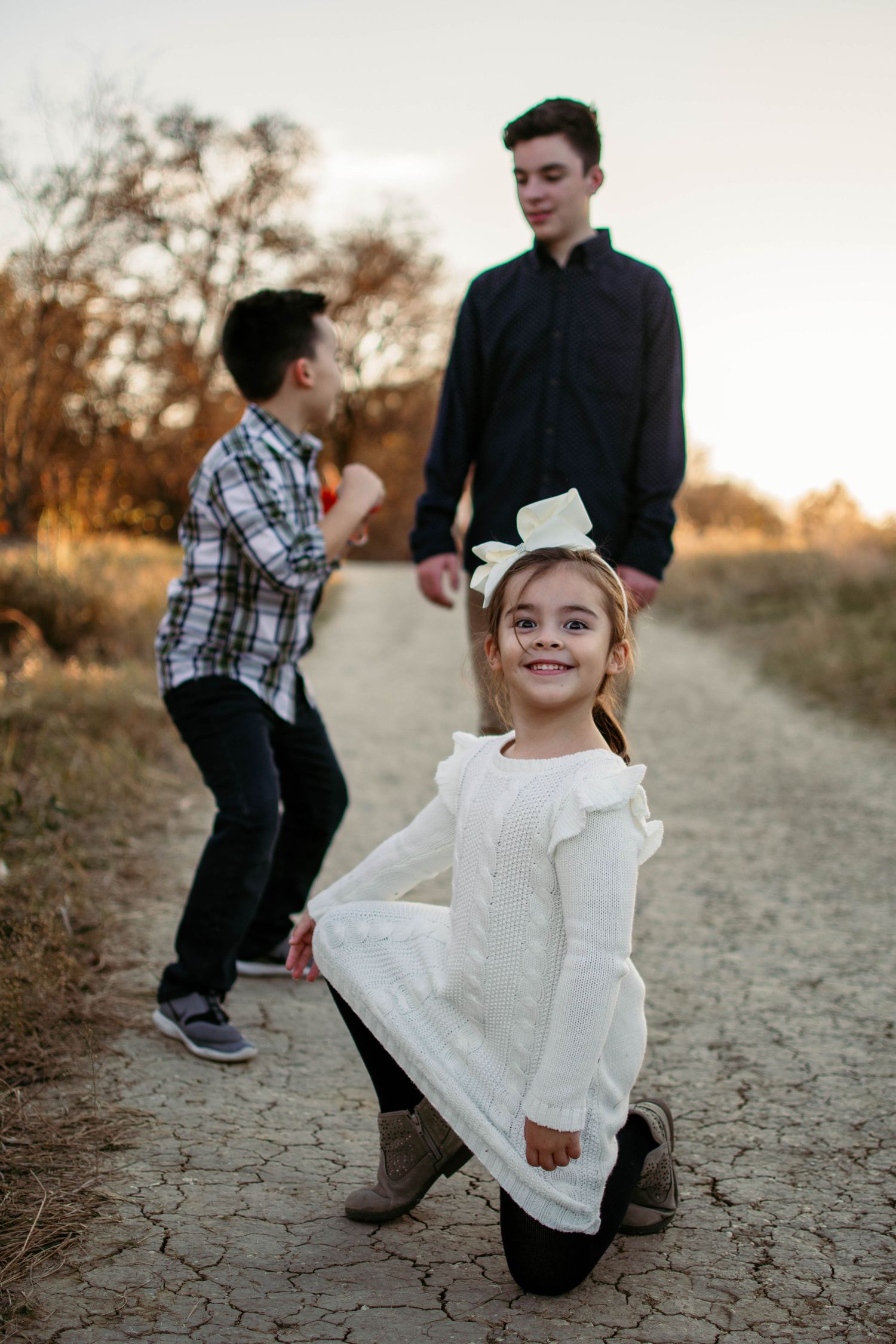 Playful outdoor portrait on a dirt path with casual poses at sunset.