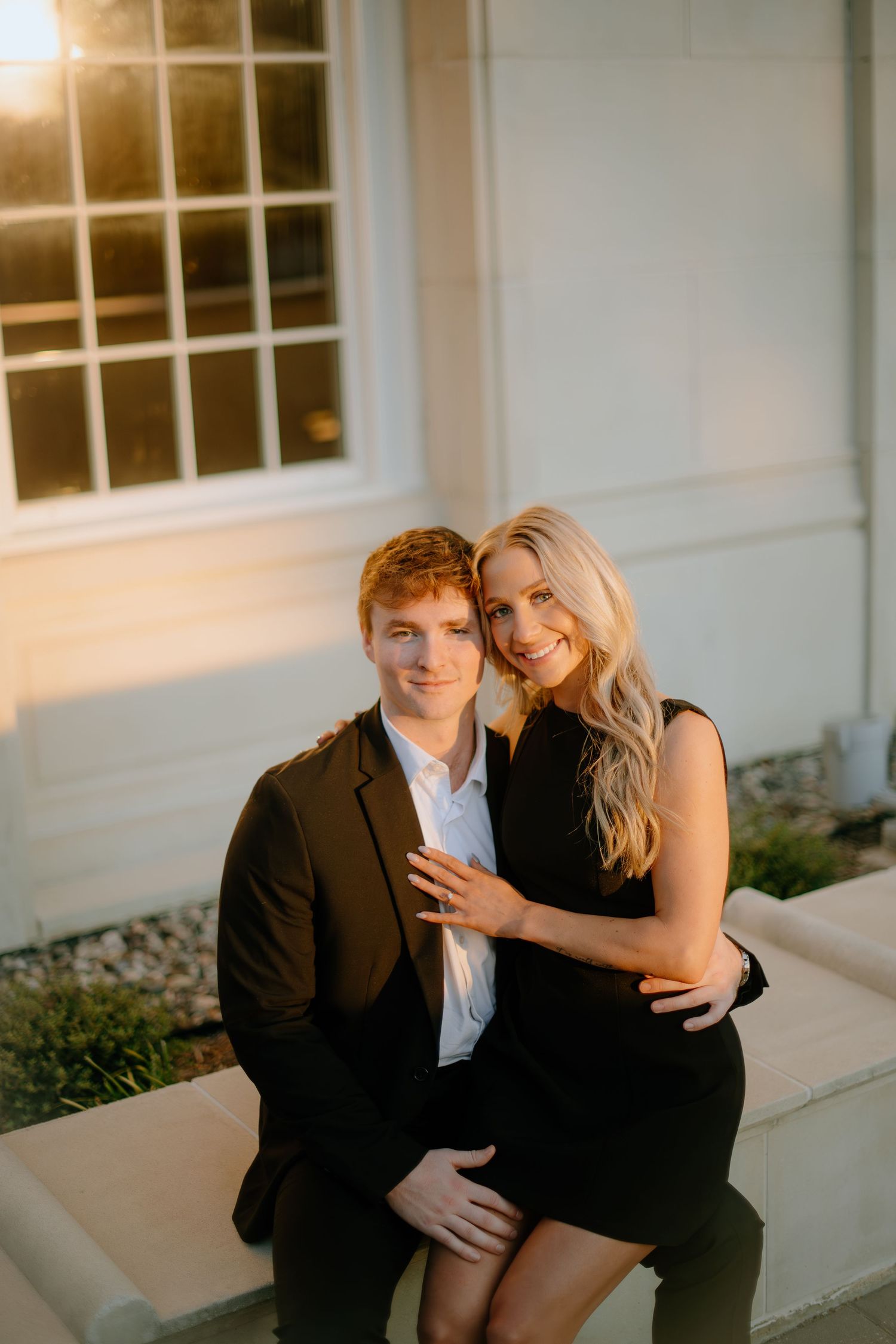 A couple shares intimate moments while posing together against a white building exterior.