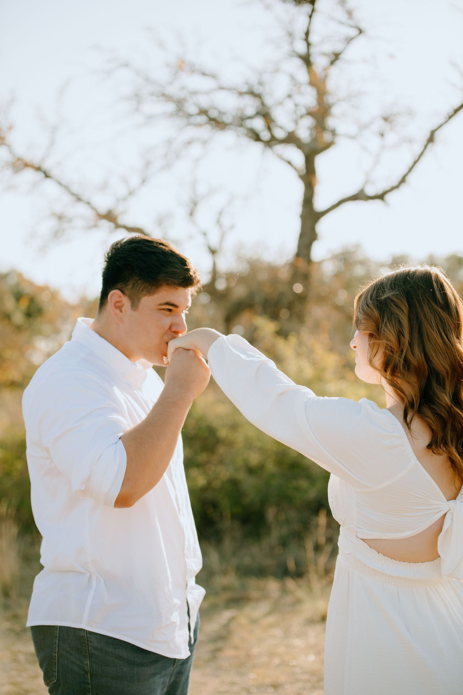 A couple in white shirts playfully dance and twirl together in a sun-drenched outdoor setting.