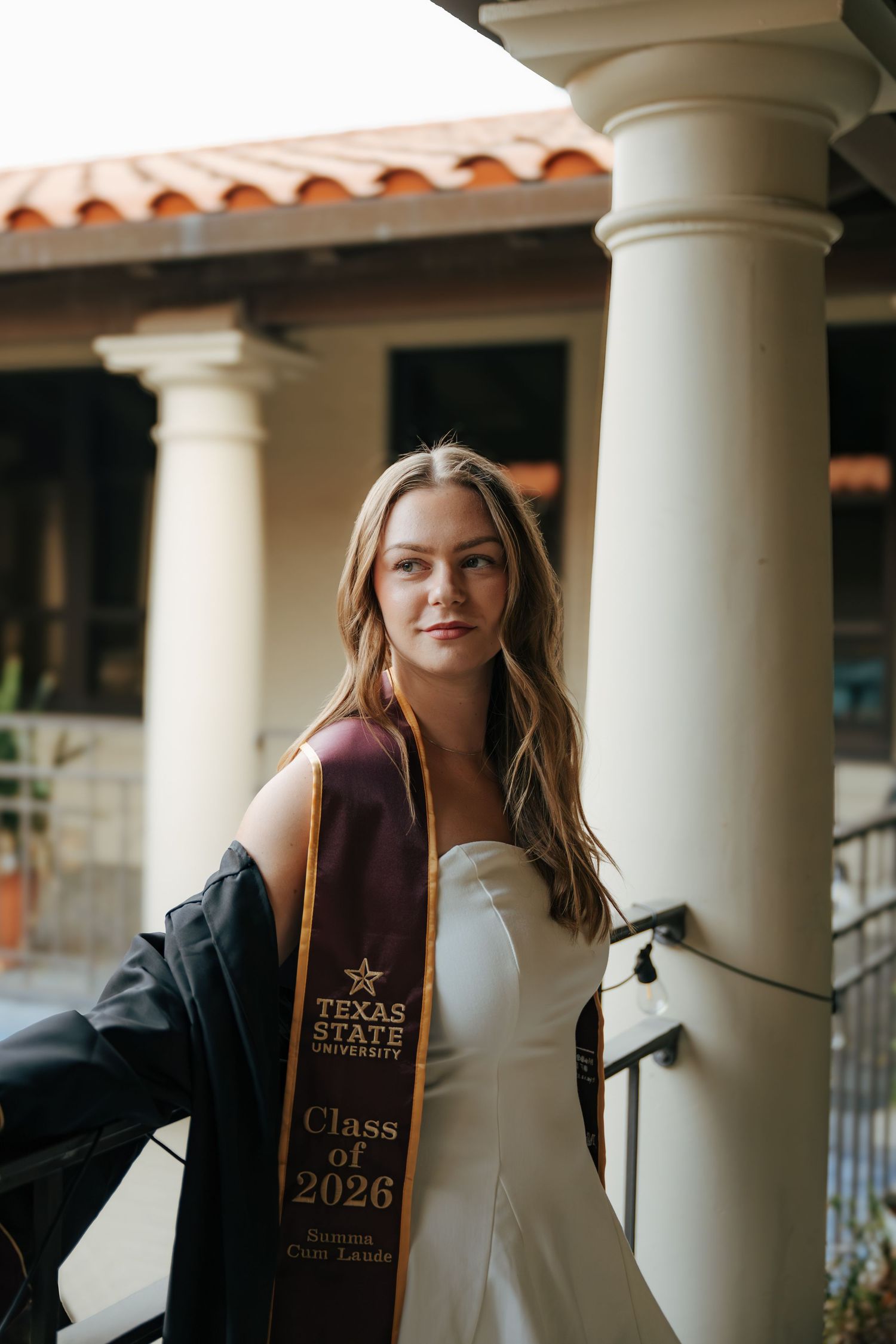 Texas State University Class of 2026 Summa Cum Laude graduate poses in white dress with maroon and gold stole.