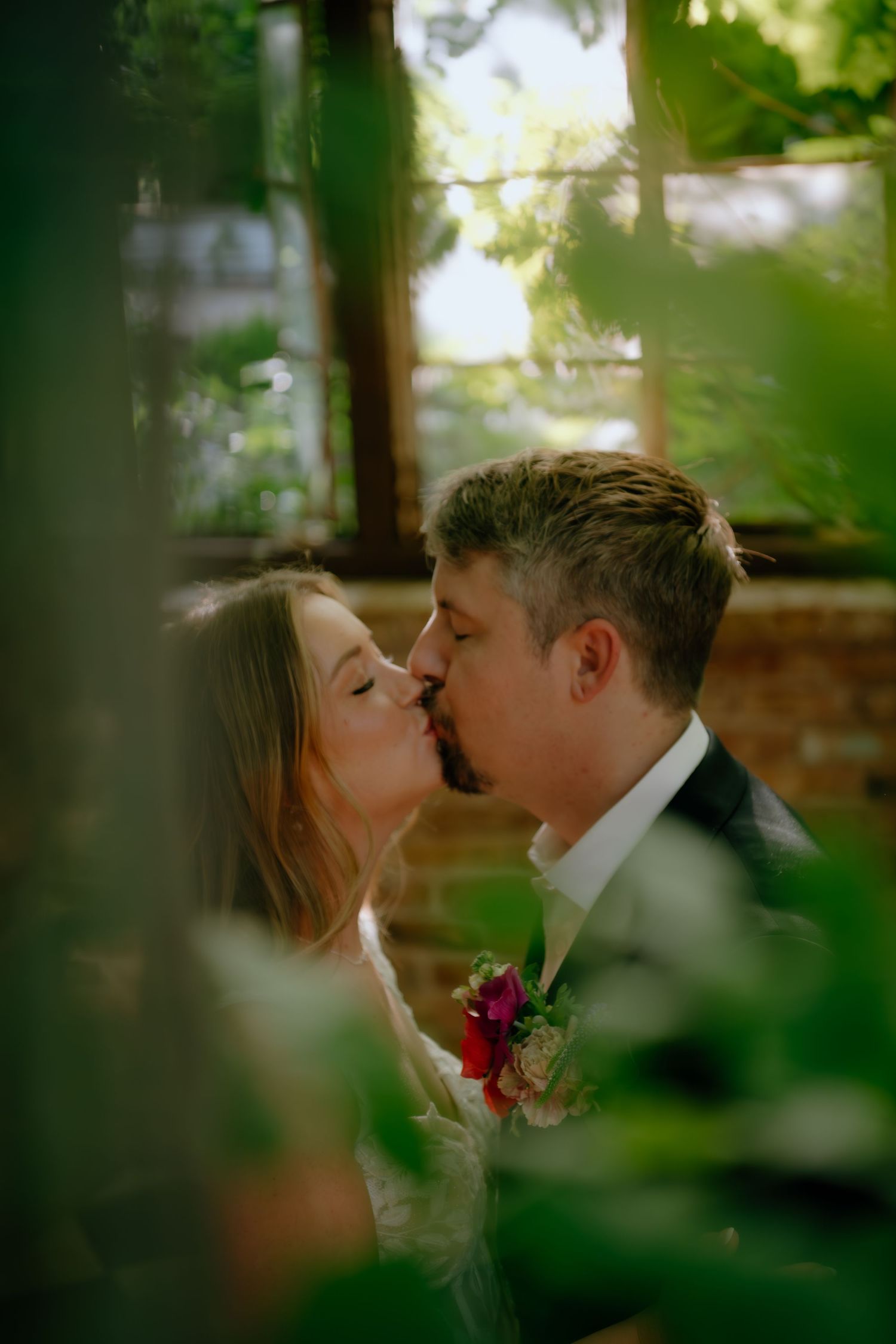 A tender kiss shared between two newlyweds framed by lush greenery.