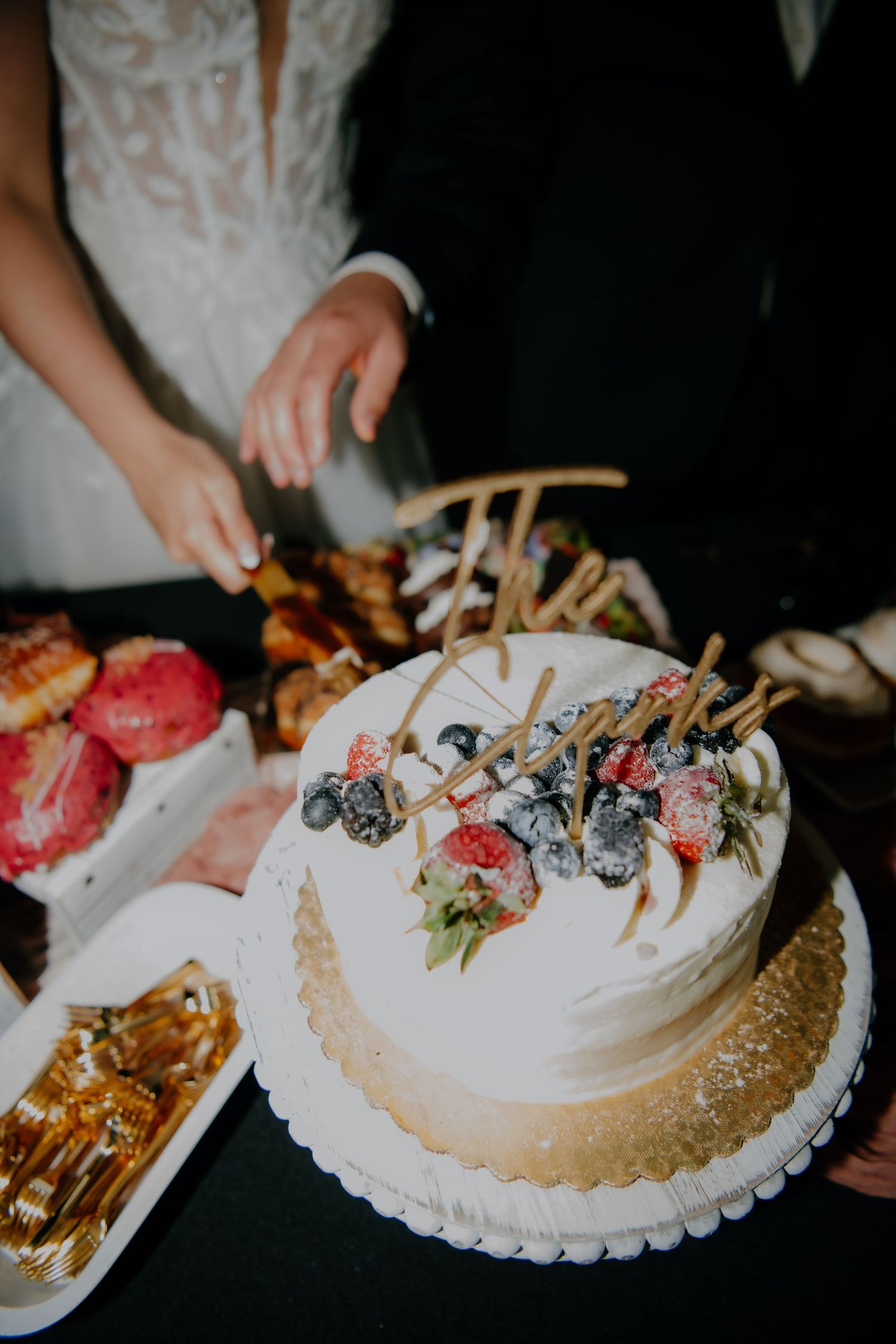 White wedding cake decorated with fresh berries and flowers on a gold cake board.
