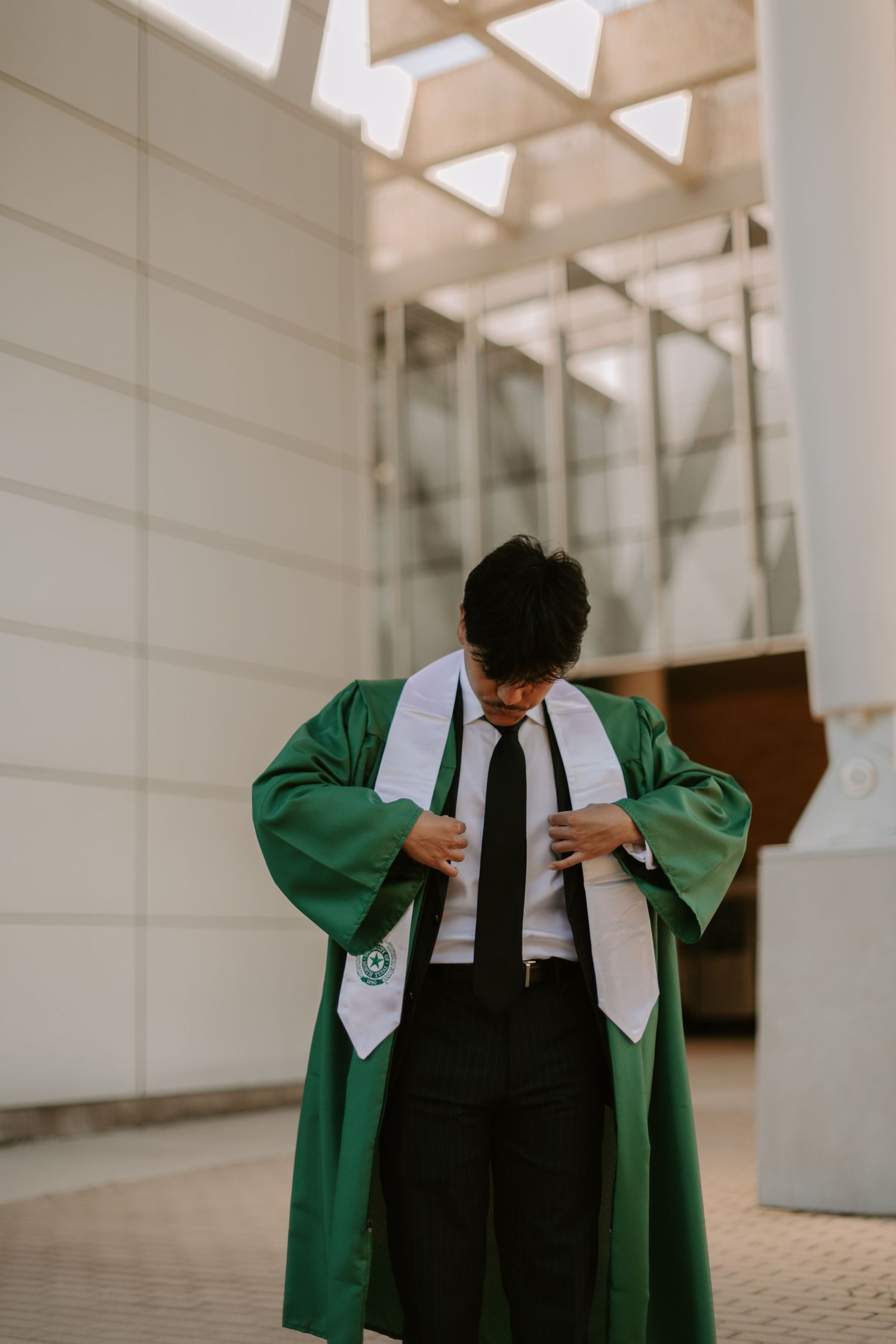 Graduate adjusts green graduation gown while standing indoors.