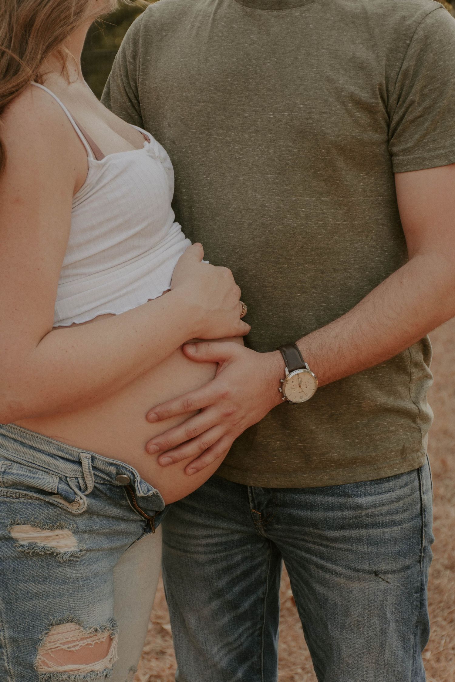 Close-up of expectant parents' hands on pregnant belly wearing casual attire.