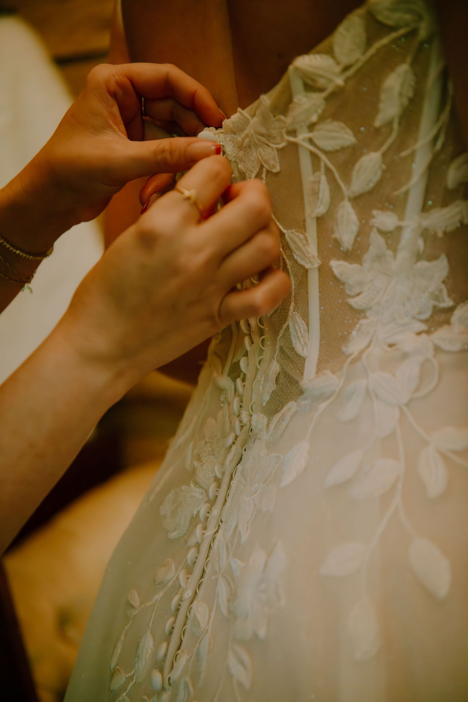 Close-up detail of hands adjusting delicate lace and floral details on a wedding dress.