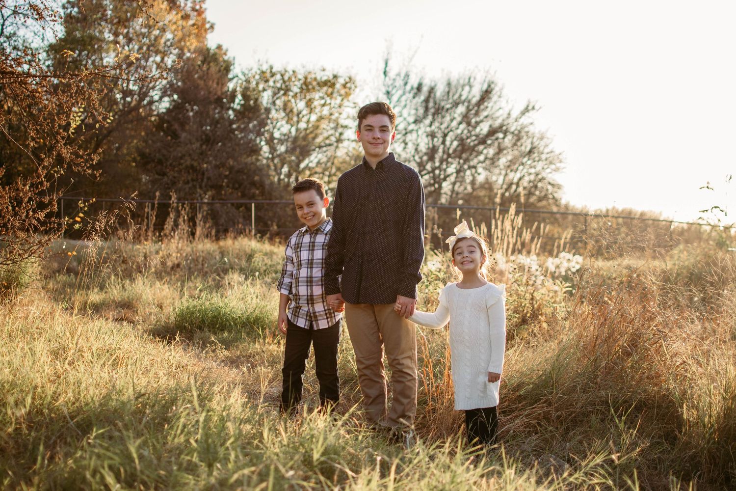 Three figures standing together in a rustic outdoor setting with warm sunset lighting.