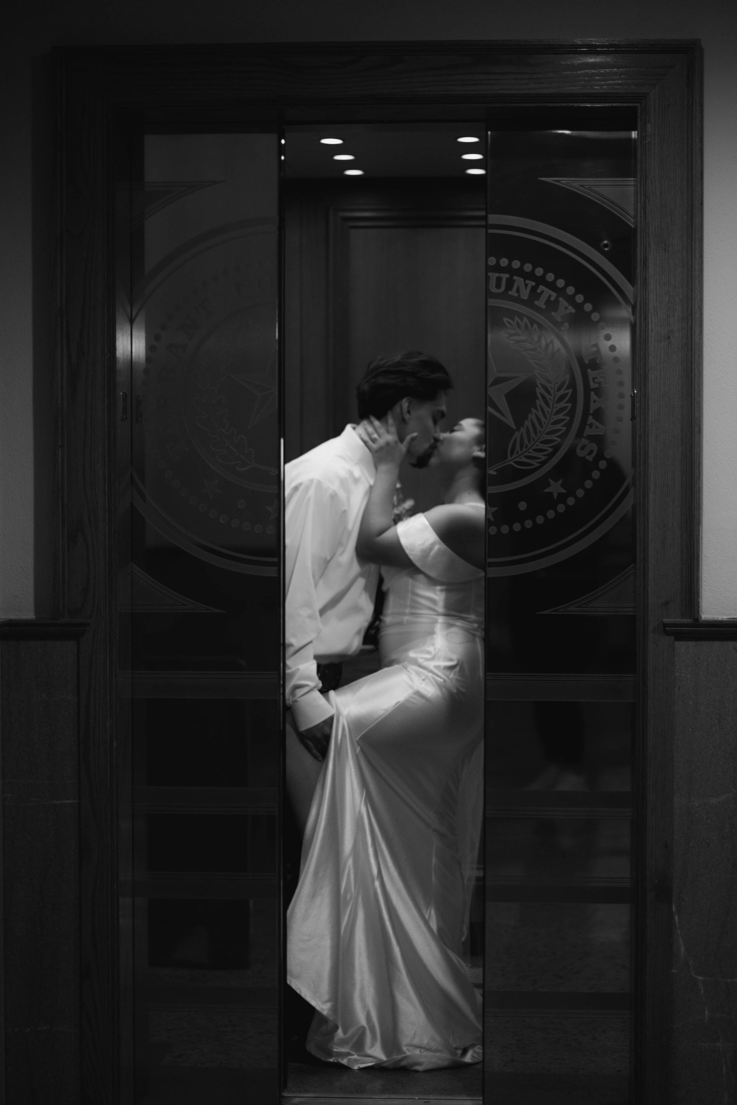 A romantic wedding couple shares an intimate moment in a doorway with an official seal visible in black and white.