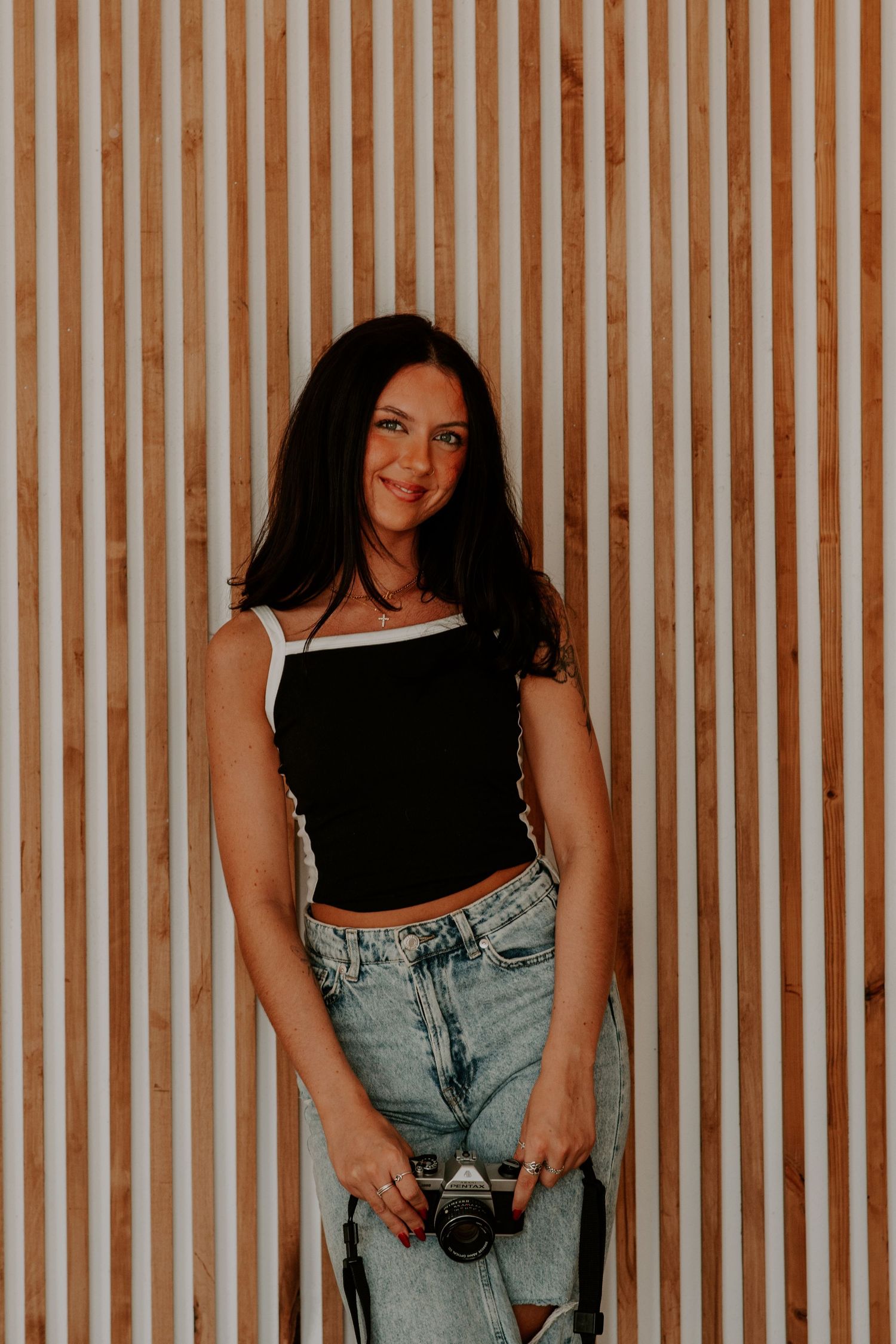Casual portrait against wooden slatted wall wearing black top and jeans.