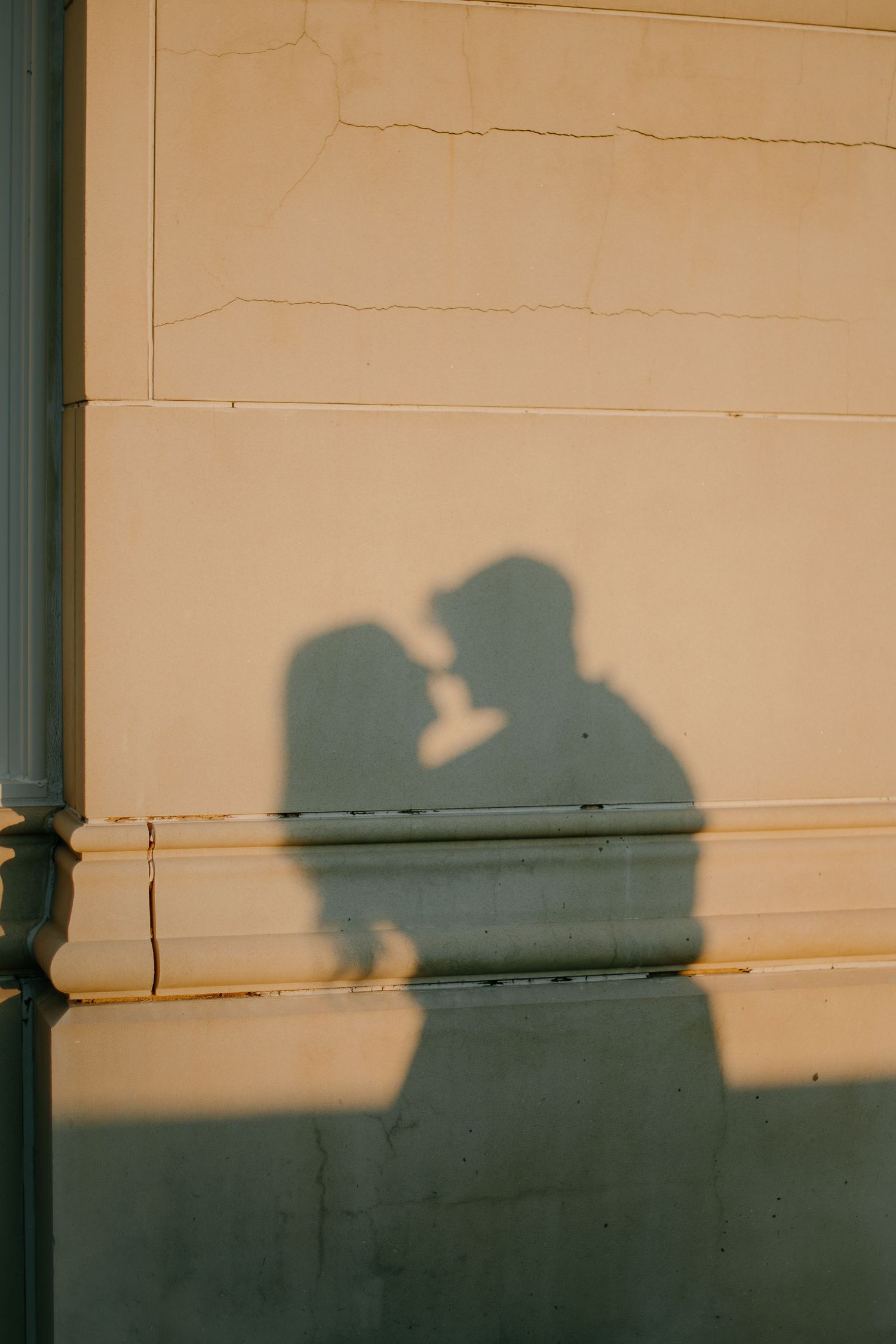 Silhouettes of people cast shadows on a beige wall at sunset creating a dramatic urban scene.