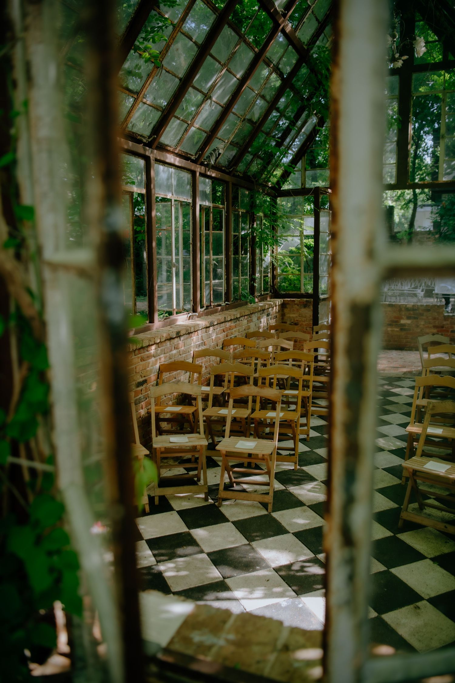 A greenhouse wedding venue with checkerboard floors and wooden chairs beneath glass windows.