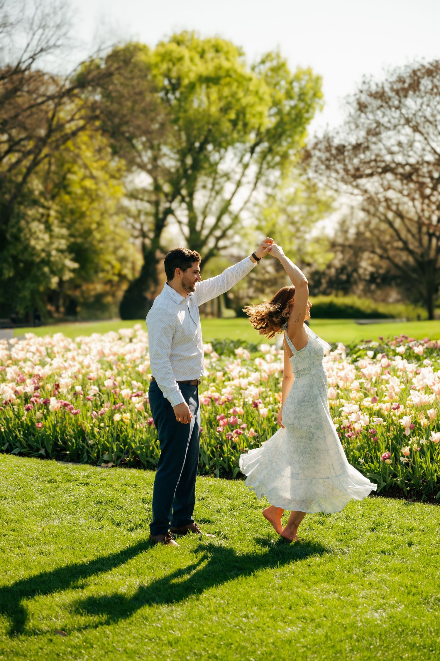 Couple dancing joyfully in a sunlit park surrounded by blooming pink and white tulips in spring.