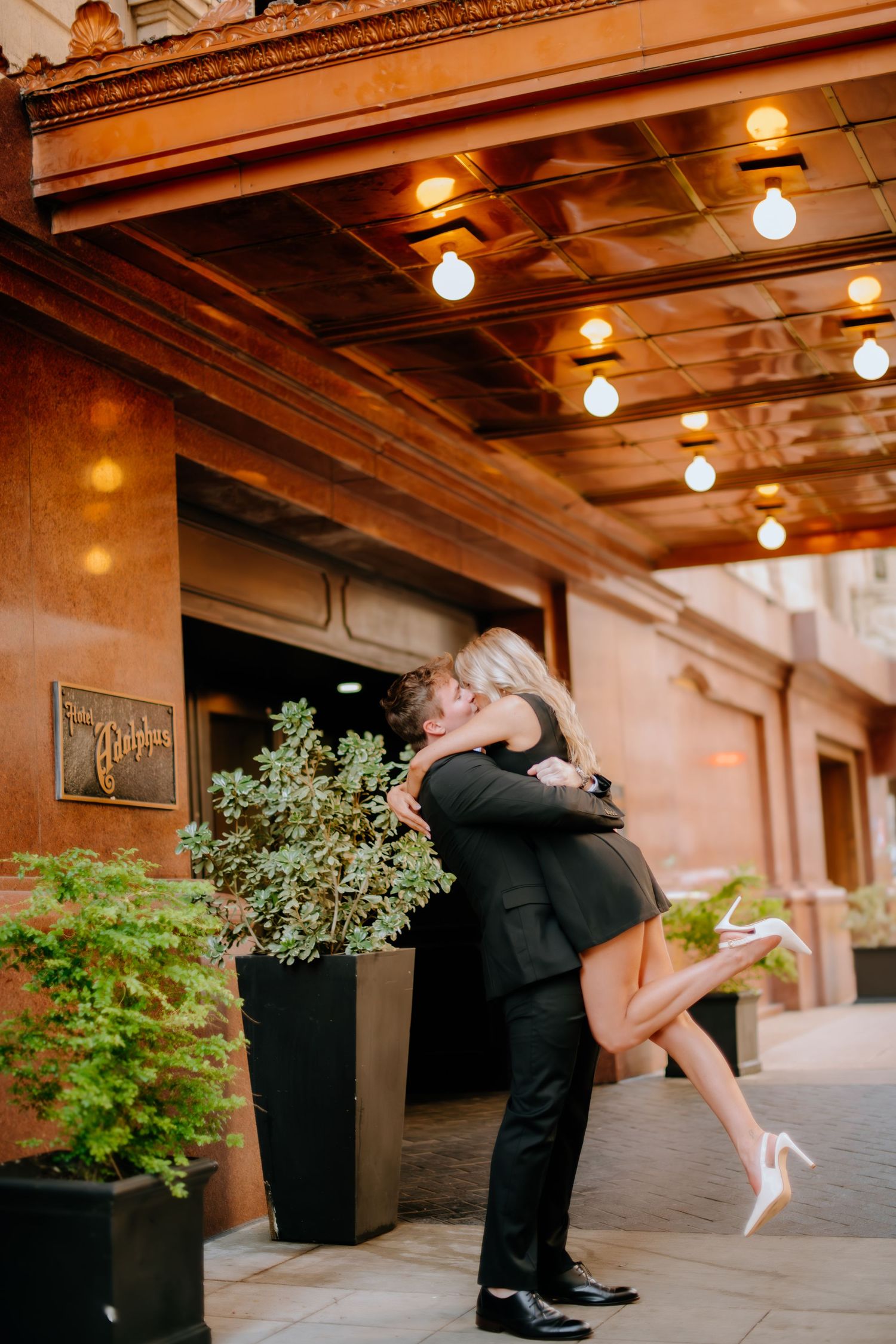 A romantic dip pose between potted plants under warm indoor lighting.