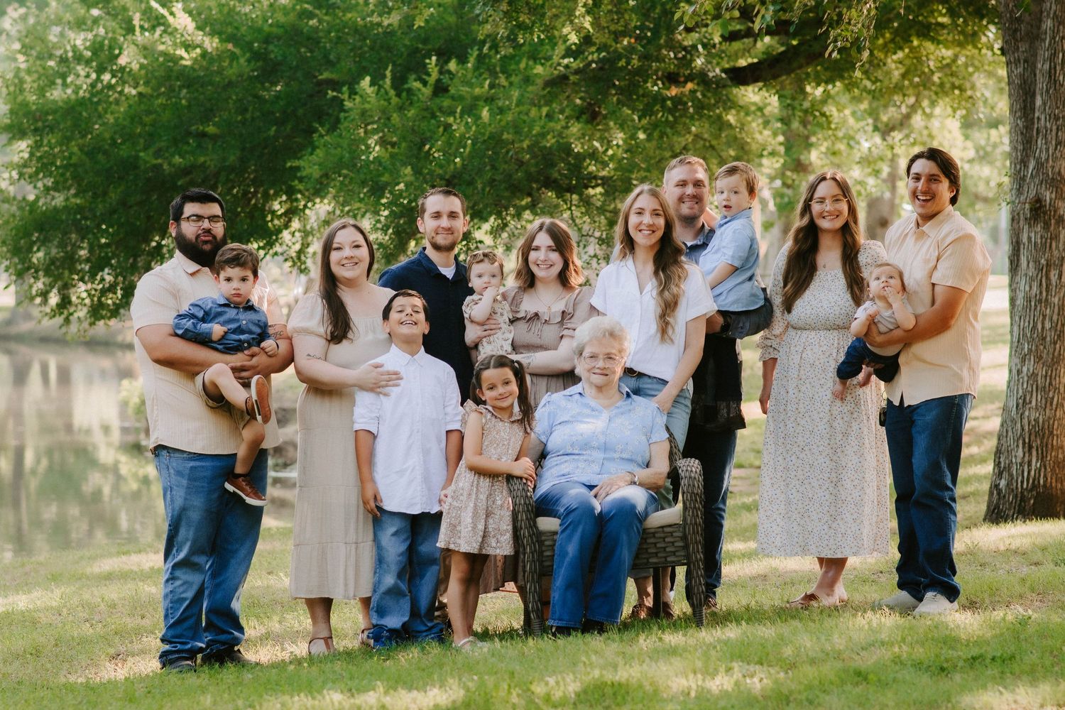 Large family group portrait outdoors by a lake wearing coordinated neutral colors.