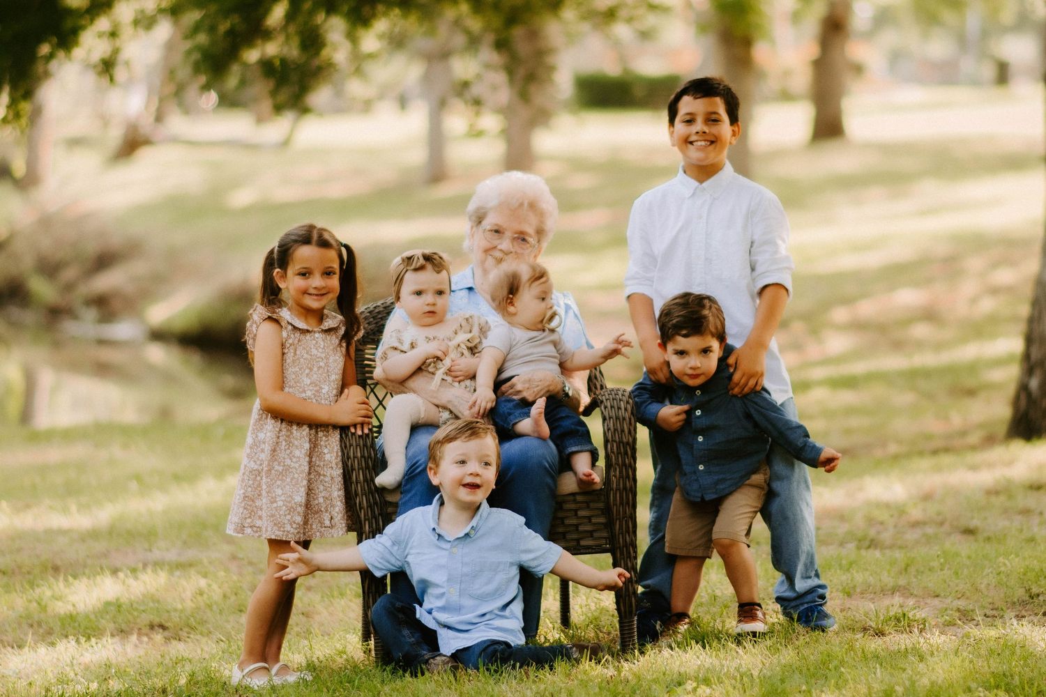 Group of children posing together on outdoor furniture under shady trees.