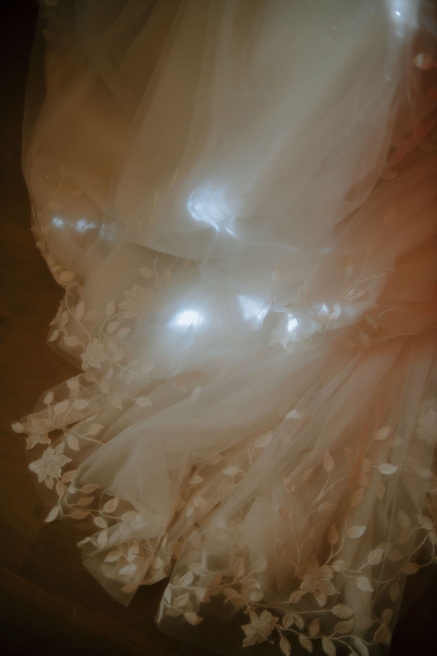 Ethereal view of a wedding dress hem with intricate floral lace details and layers of tulle.