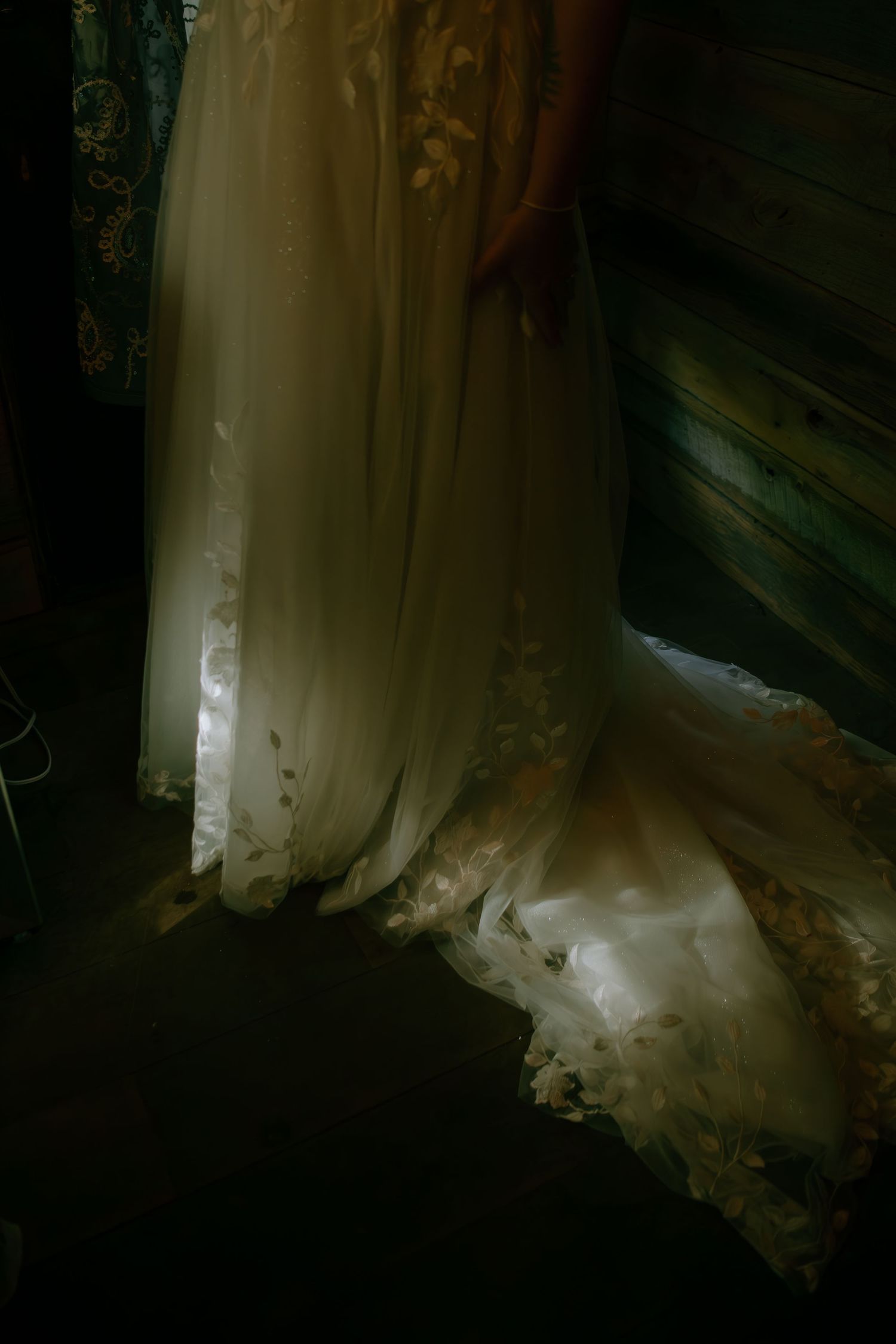 Ethereal wedding dress with lace hem pooling on floor in dramatic dark moody lighting.
