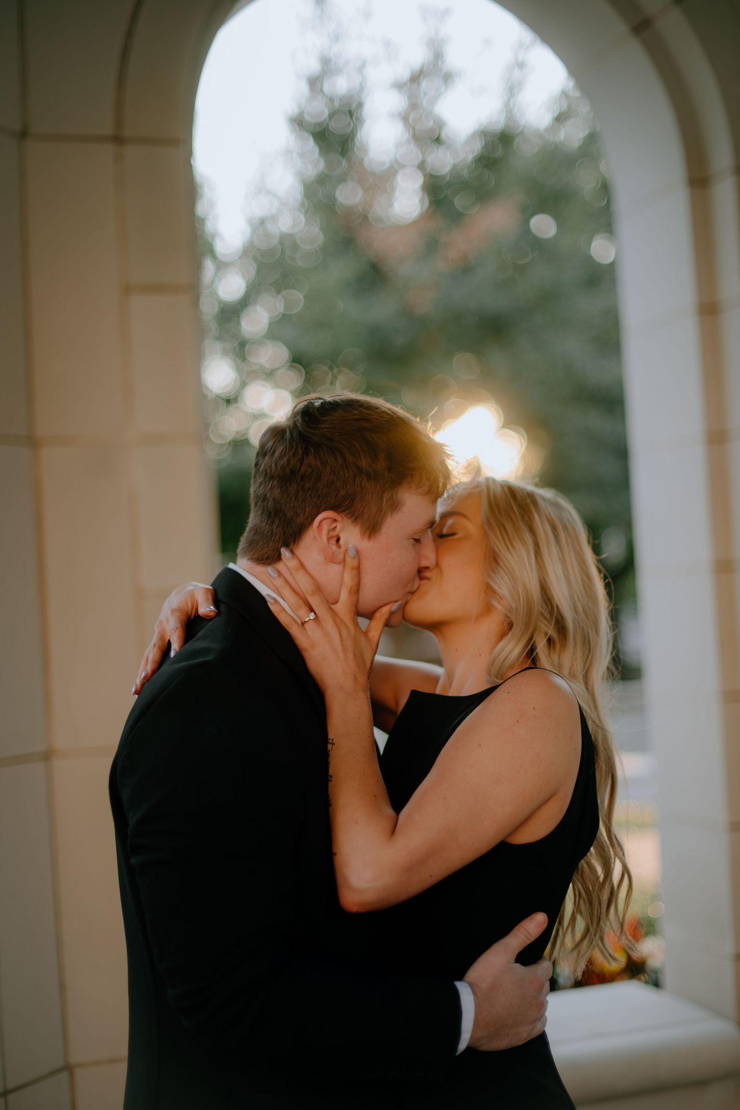A romantic couple shares a tender kiss under an arched walkway during golden hour.