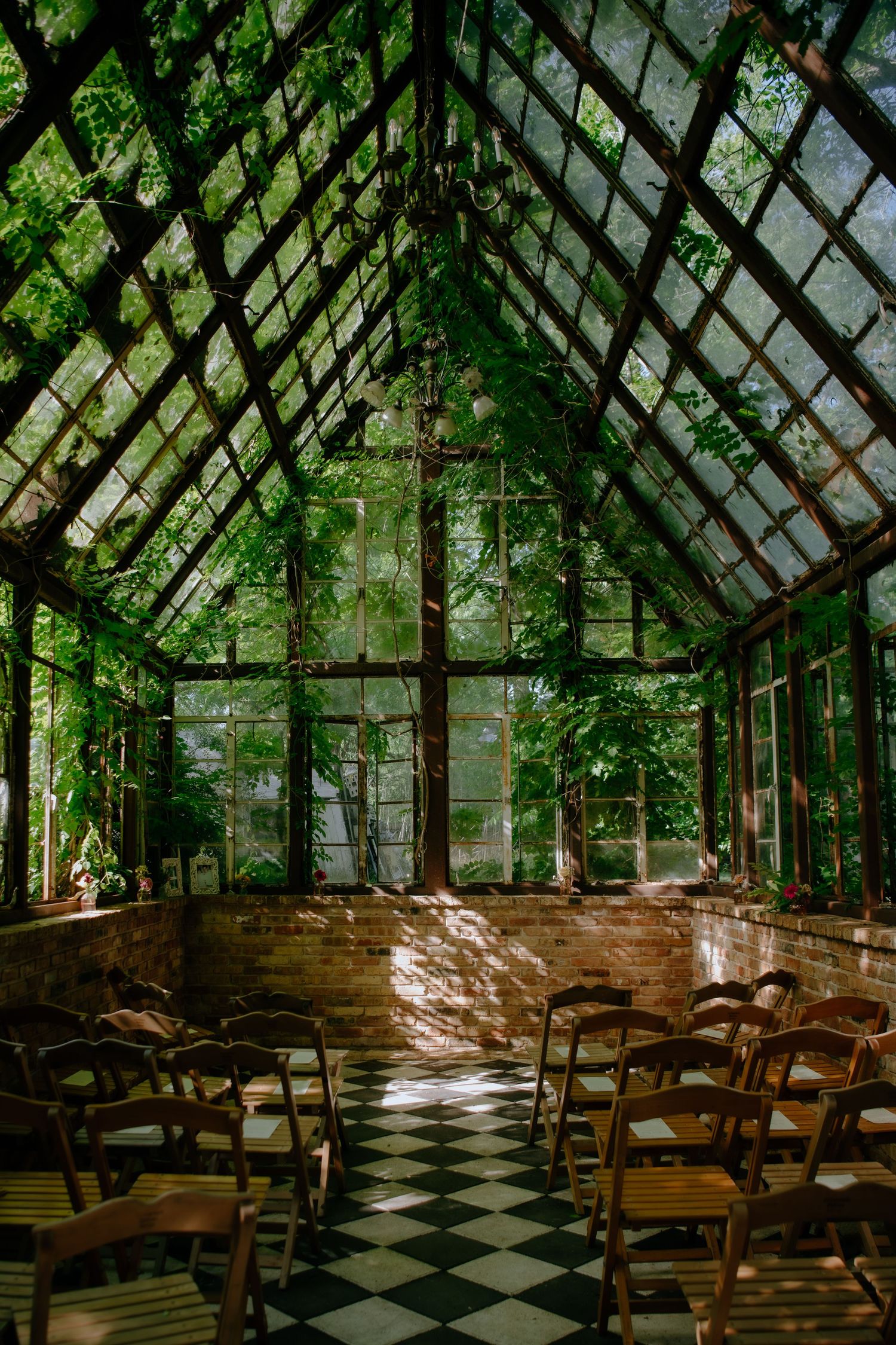 Sunlight streams through a glass greenhouse chapel with wooden chairs arranged for a ceremony.