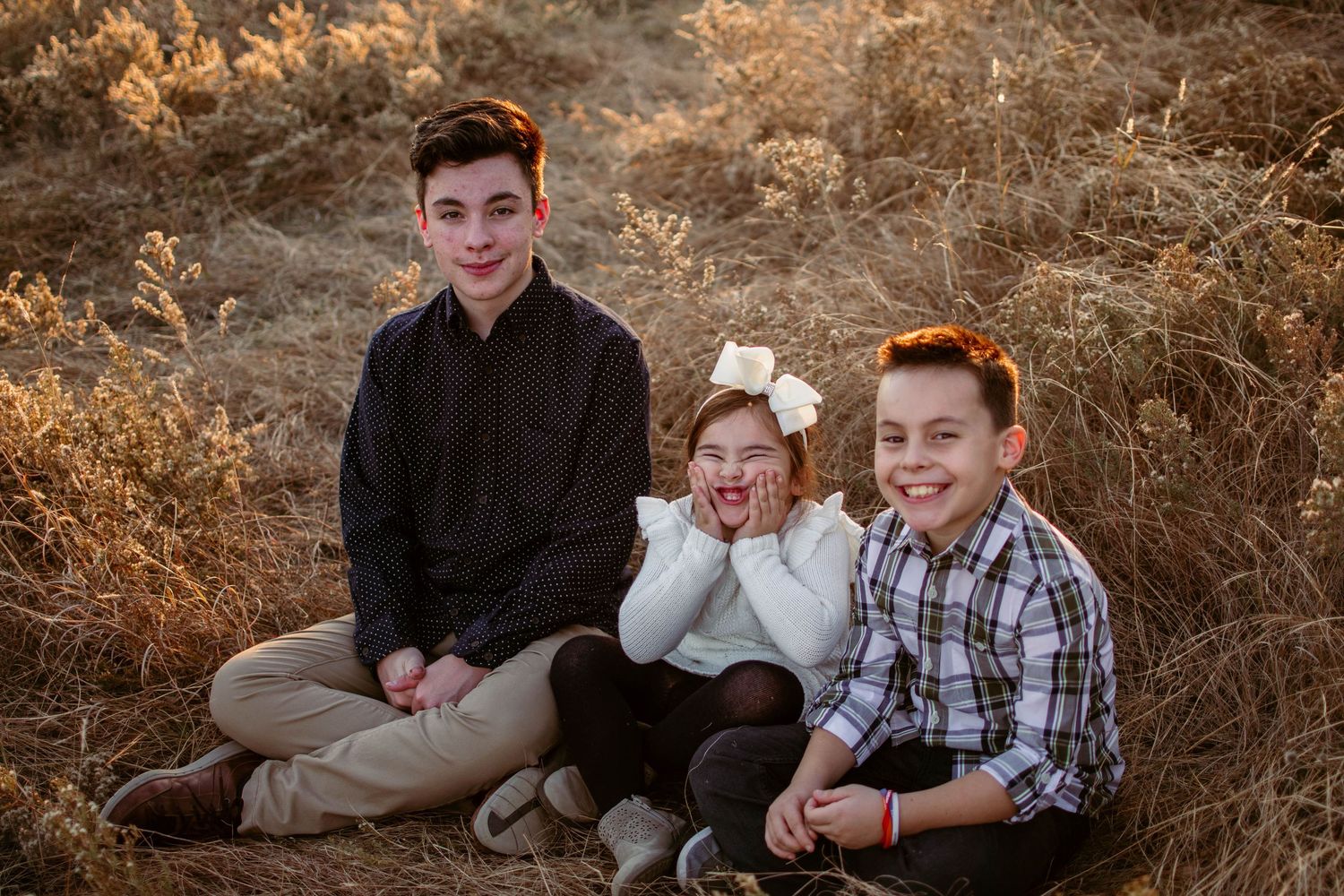 Candid sitting portrait in golden field during sunset hours.