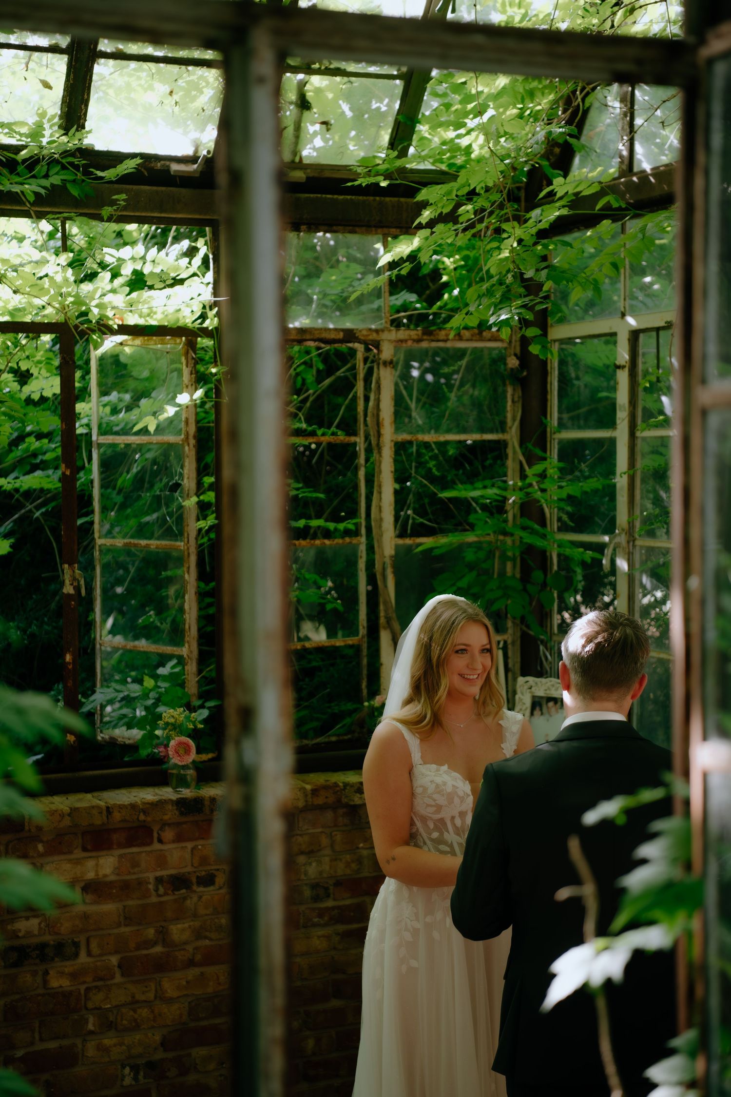 Wedding ceremony in a greenhouse with lush greenery and brick walls.